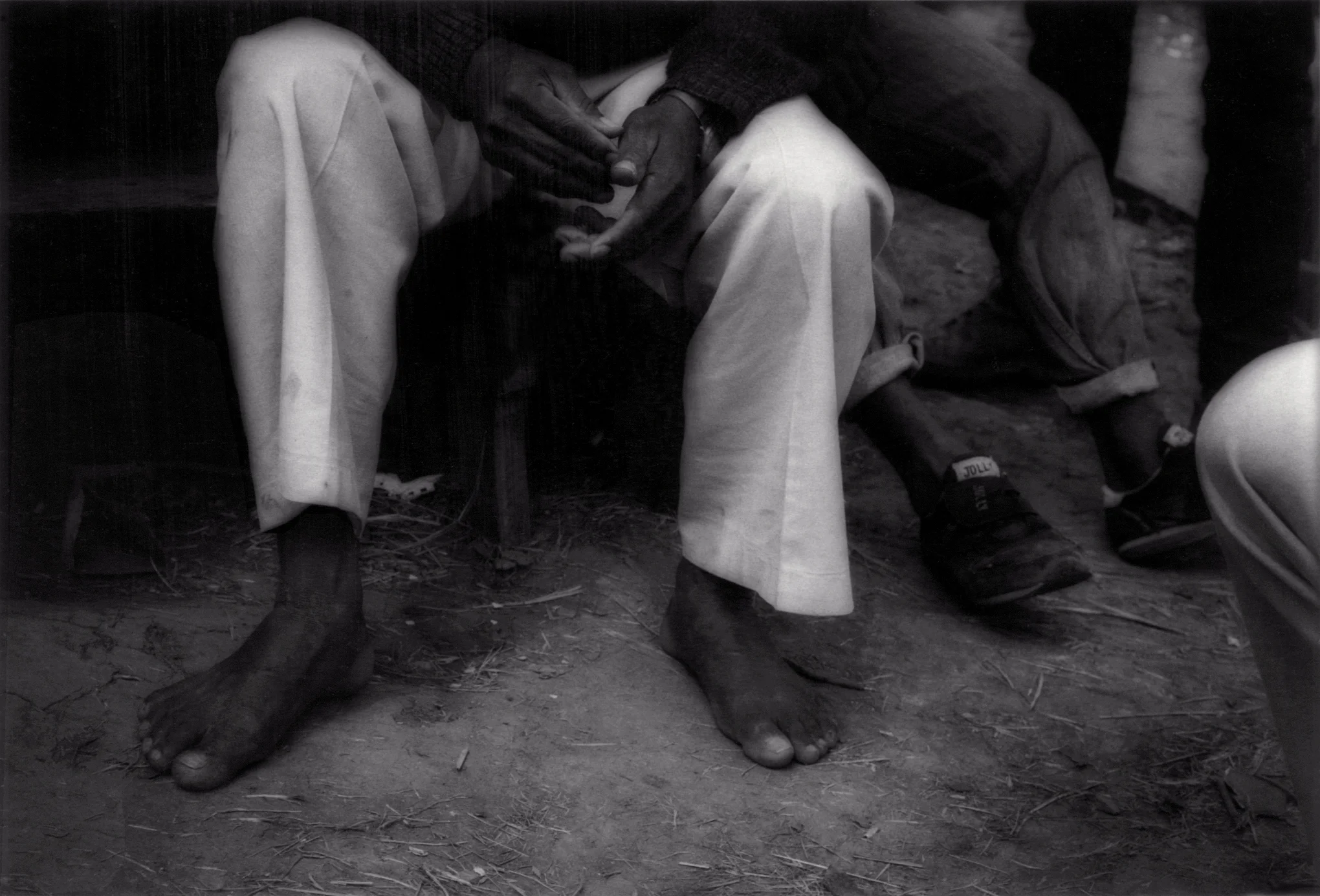Migrant farm worker's feet sitting before his makeshift house, in 2006, in a remote canyon beside agricultural fields in rural northern San Diego County, California, USA.