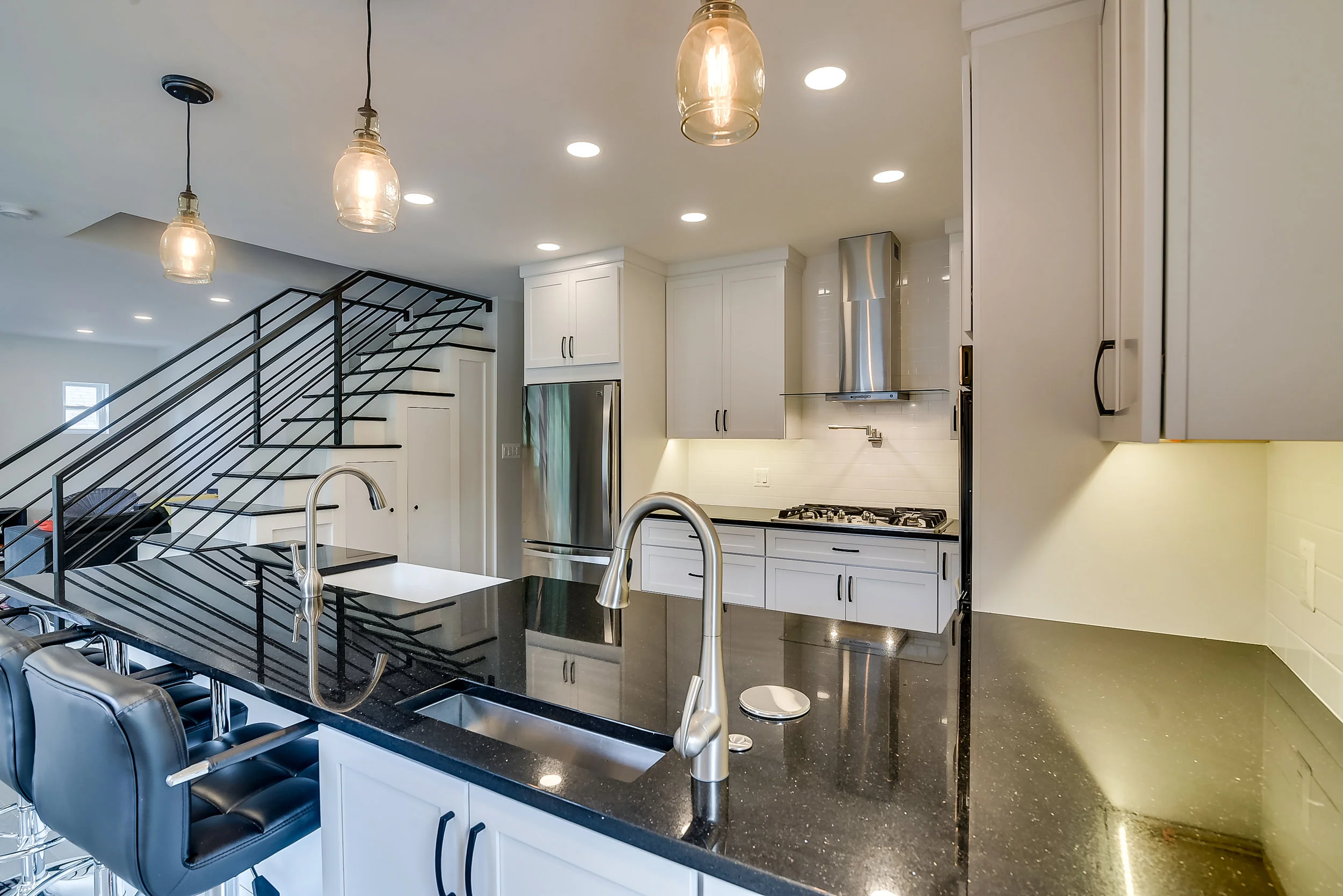 White kitchen with black countertops pendant lights and metal stair railing.jpg