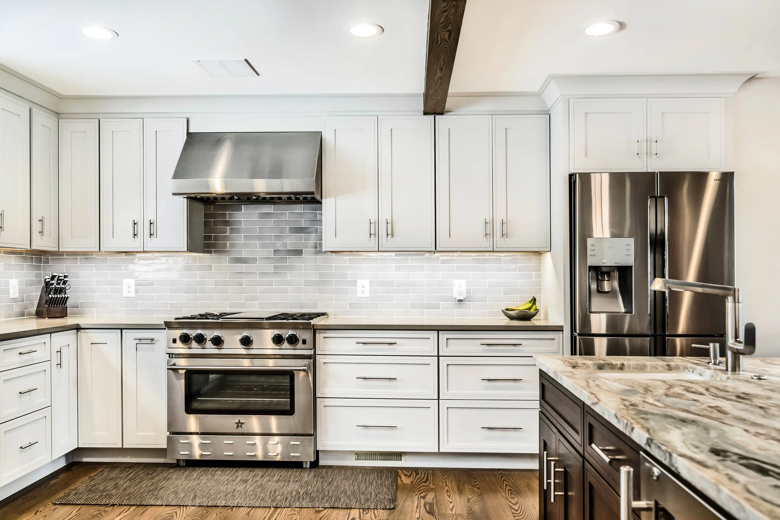 White kitchen cabinets with stainless steel range gray tile backsplash and wood ceiling beam.jpeg