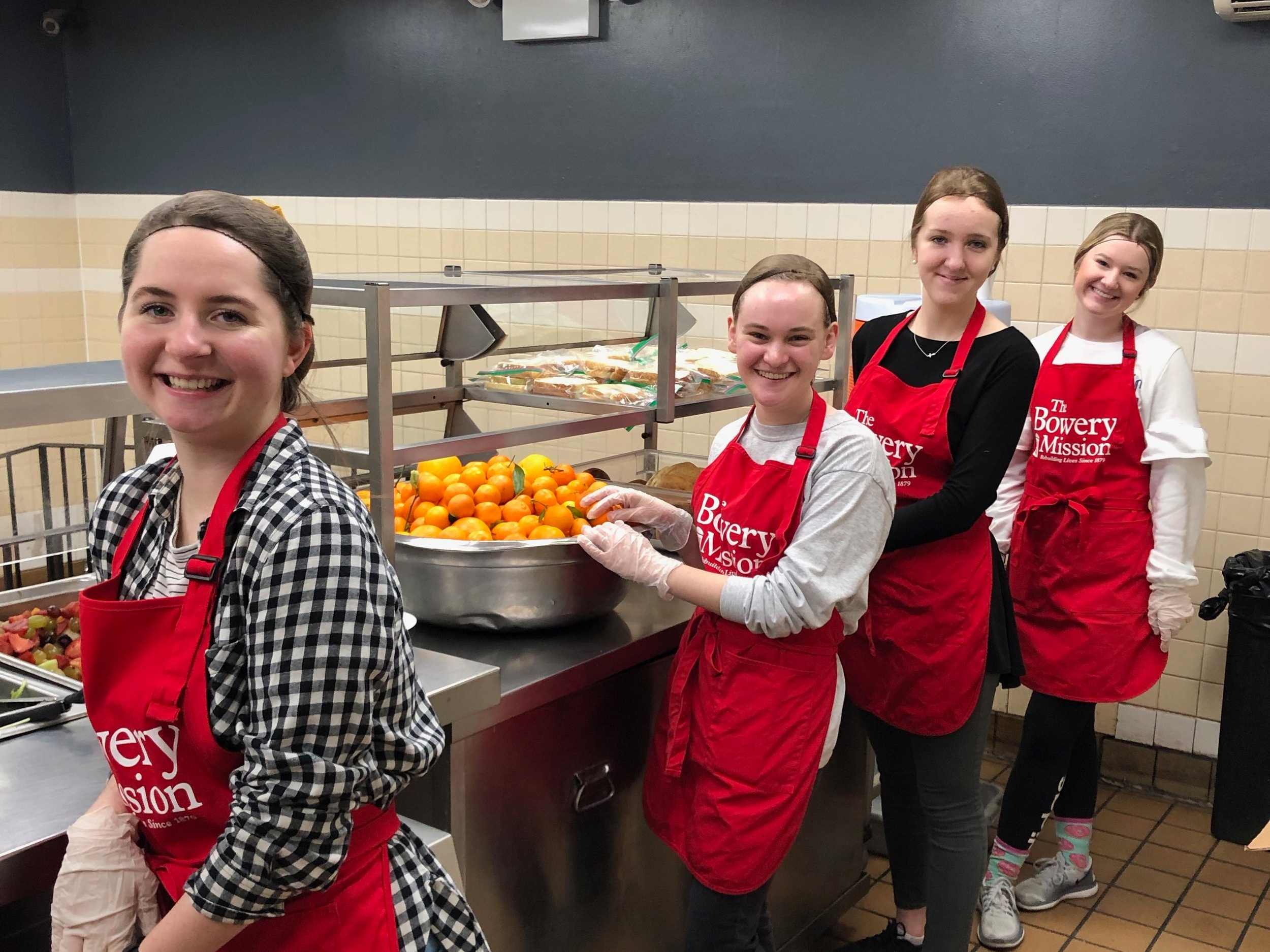 (Left to right): Lydia Marlin, Elise Wharton, Dominique Lacroix, and Abigail Wells are stationed in the kitchen at The Bowery Mission getting ready to serve. || Photo credit to Serena Tuomi.