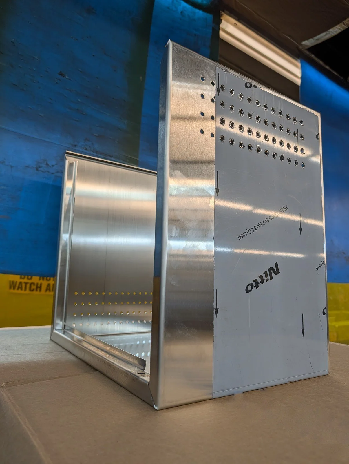 Formed stainless steel enclosure with punched perforation pattern and protective film