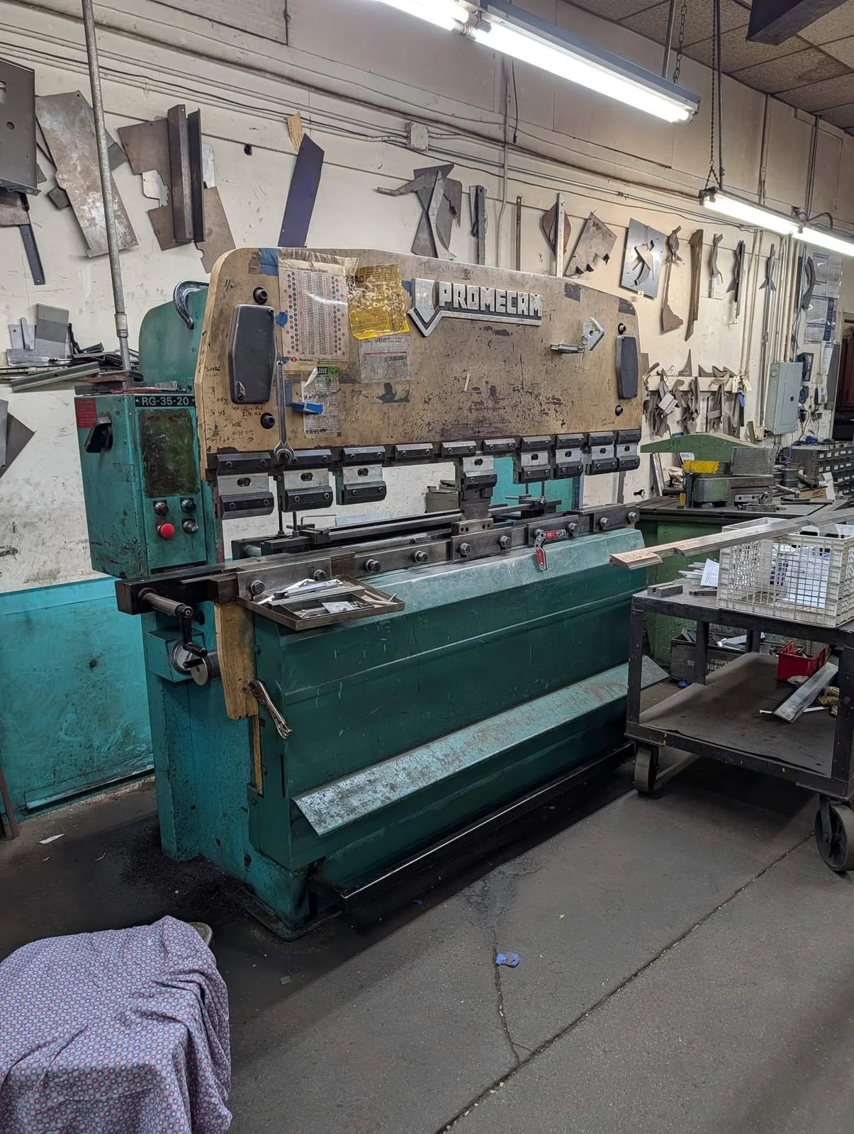 Press brake with tooling and a rack of bending dies on the wall