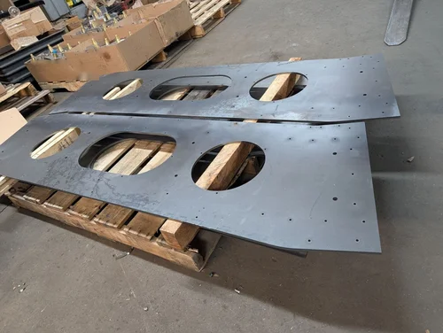 Two large laser-cut steel plates with round and oval cutouts on a pallet