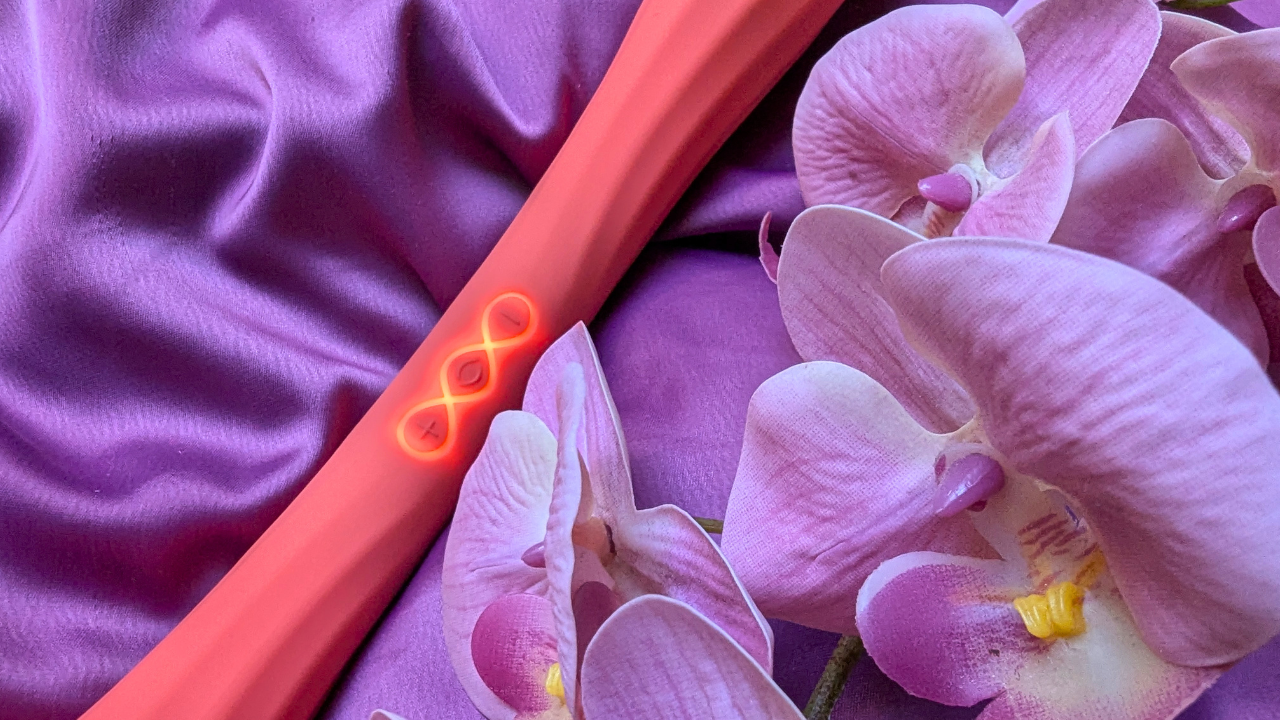 close up of LELO Boomerang double ended vibrator in coral red next to some orchids