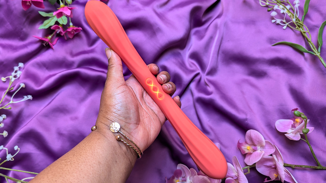 black woman's hand holding LELO Boomerang double ended vibrator in coral red whilst on