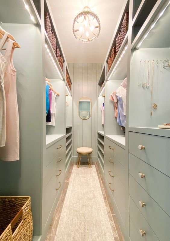a-mint-green-narrow-closet-with-lots-of-drawers-and-open-storage-compartments-with-lit-up-shelves-and-a-chandelier.jpg
