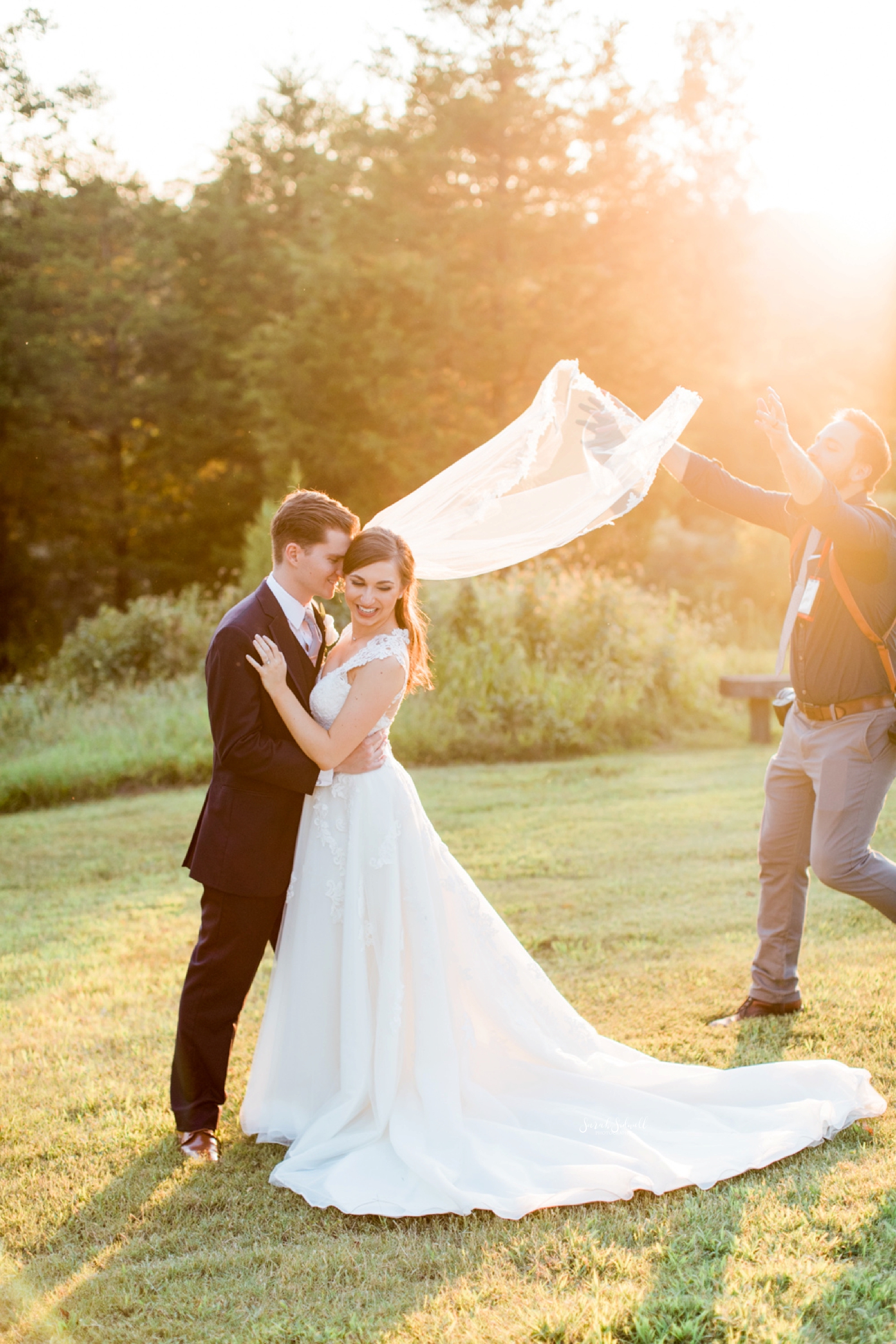 A photographer holds a bride's veil for a photo.