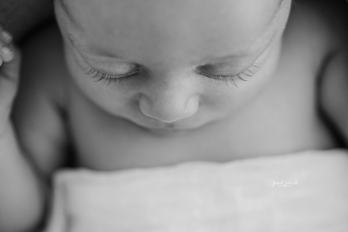 A baby sleeps while covered in a white blanket.