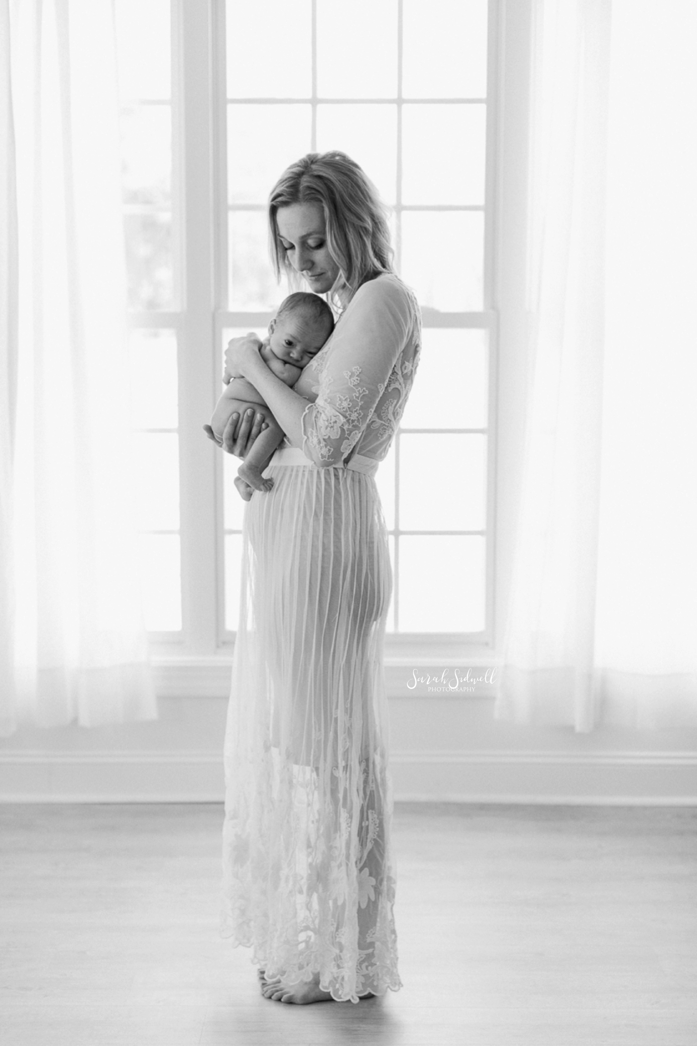 A mother dances with her newborn baby by a window.