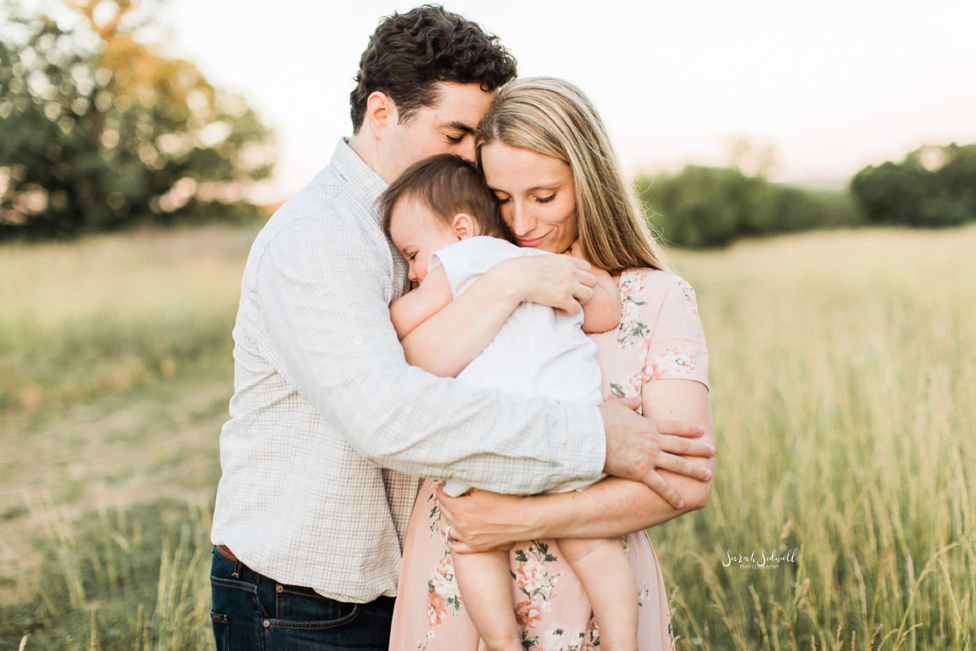 A man wraps his arms around his wife and baby boy.
