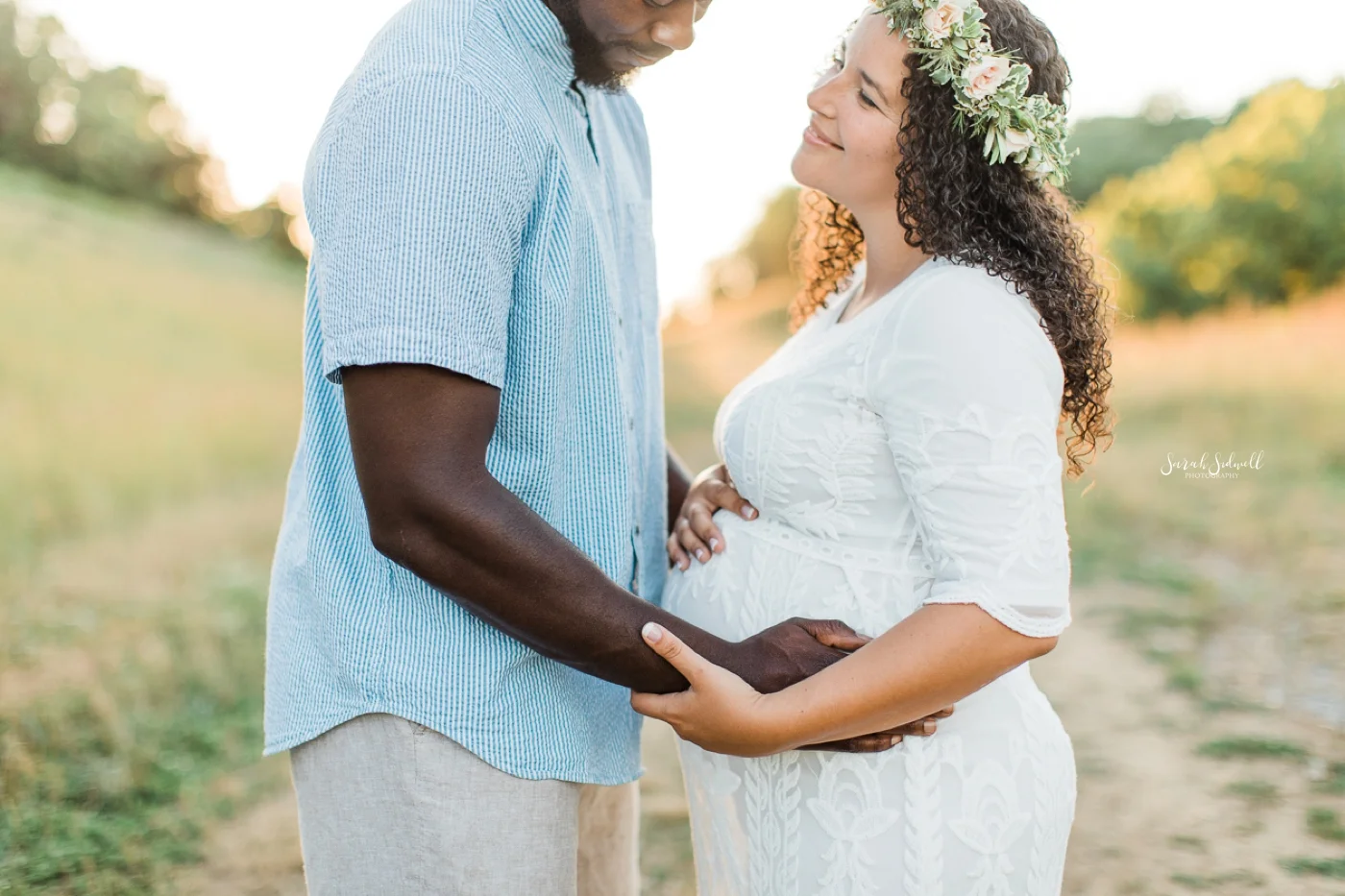 A man holds his wife's pregnant belly in front of a sunset.