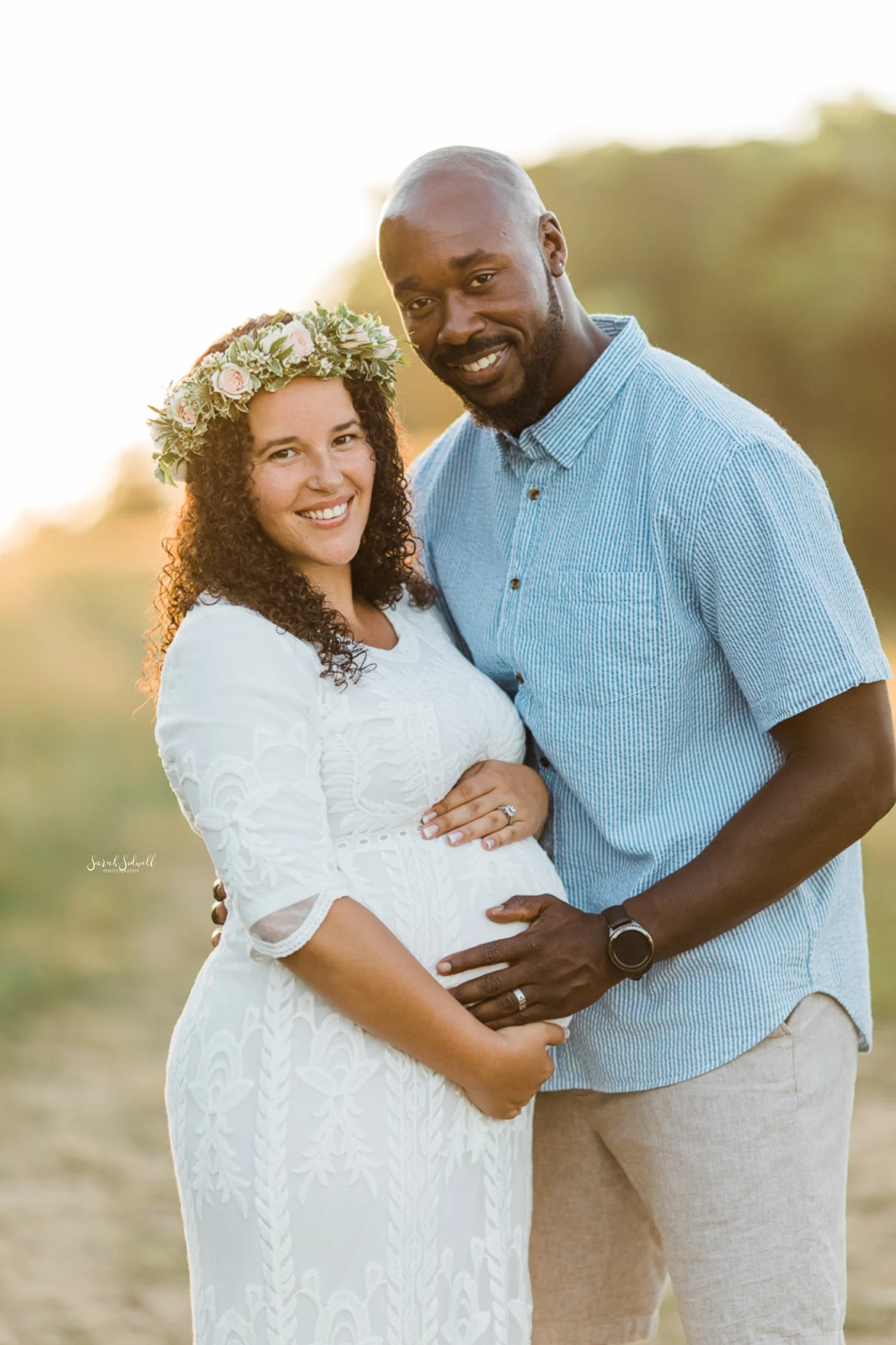 A pregnant woman wearing a flower crown stands with her husband.