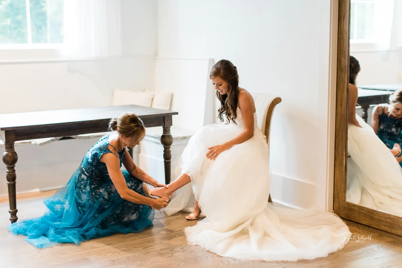 A bridesmaid helps put on a bride's shoe.