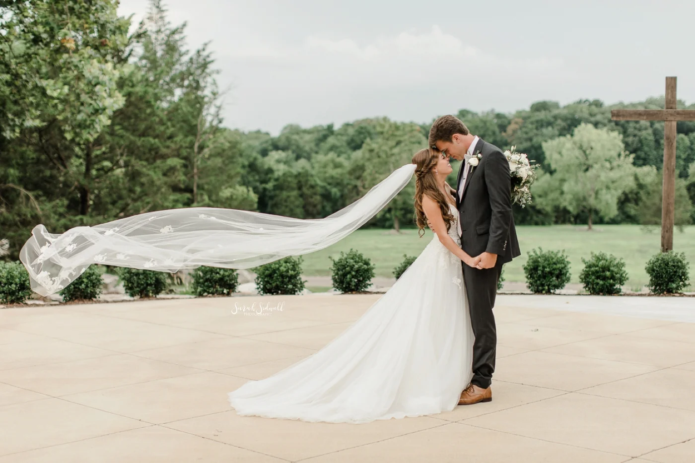 A bride's veil blows in the wind as she kisses her groom.
