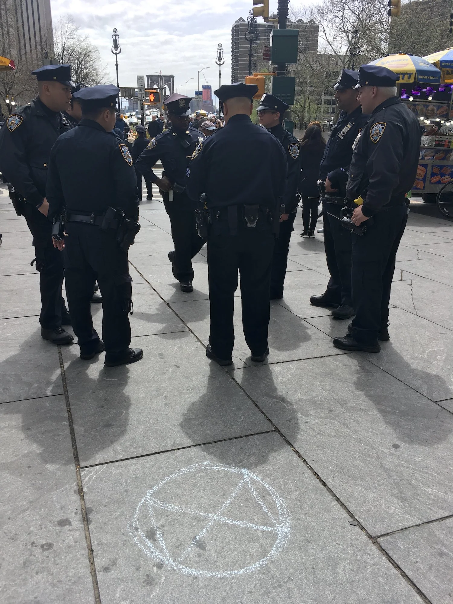 Circles of power: Extinction Rebellion logo and a group of NYPD, Brooklyn Bridge in background