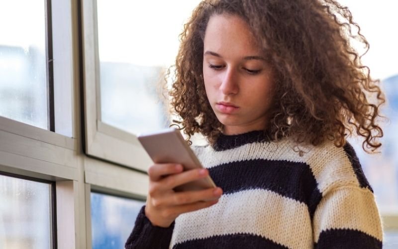 En flicka som håller i en mobil. Gestaltar ett uppdrag via mobilen.