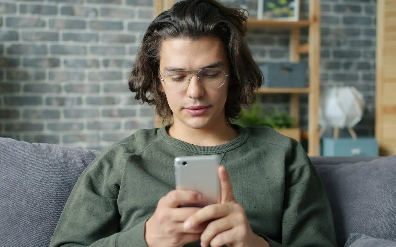 Ungdom sitter i en soffa  med en mobil