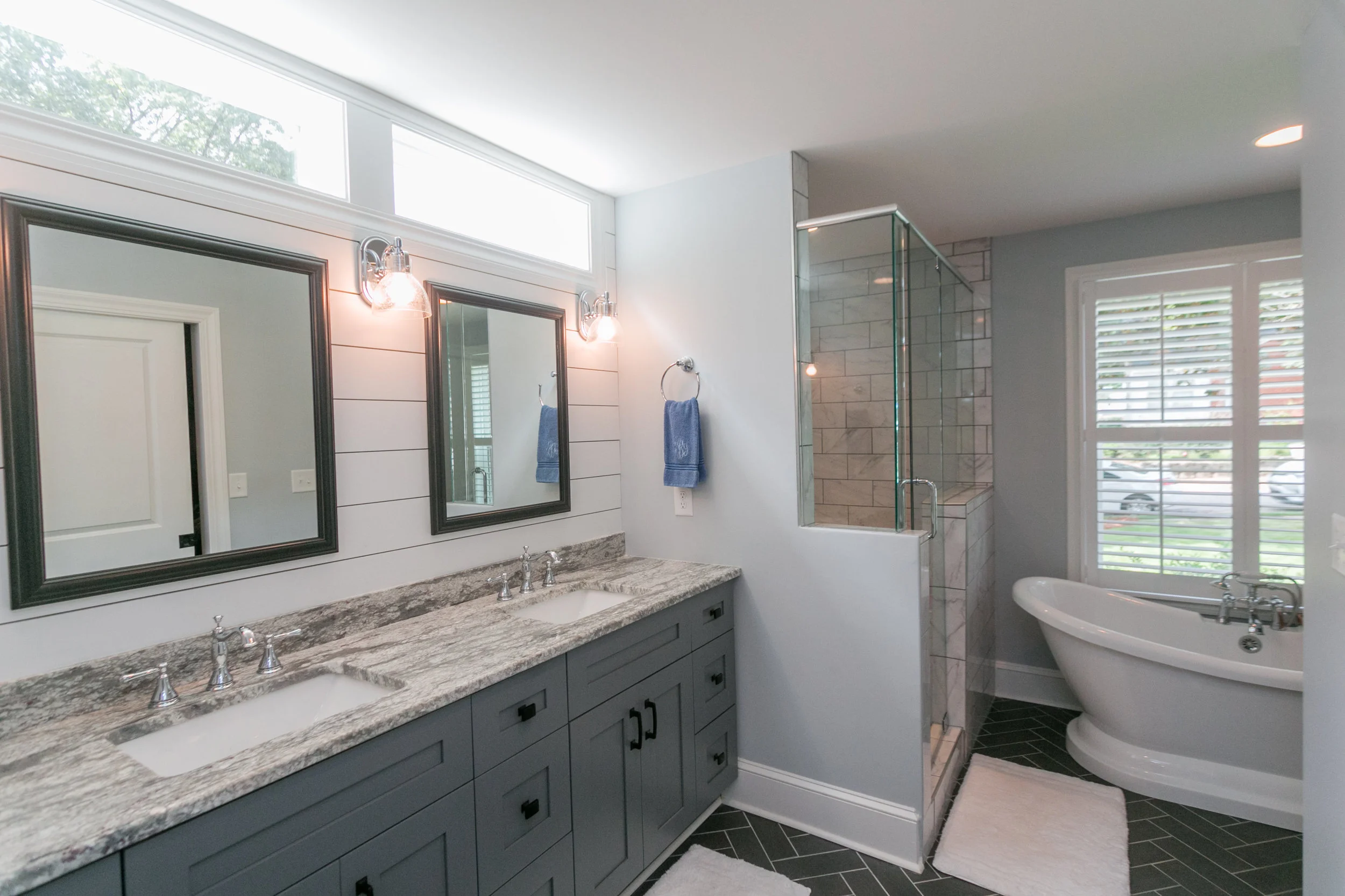 The master bath balances the perfect amount of natural light. Adding transoms above the vanity frames each of the sinks. The back wall accent is painted reclaimed shiplap. The floor tile includes a herringbone floor tile pattern. The mix of chrome a…