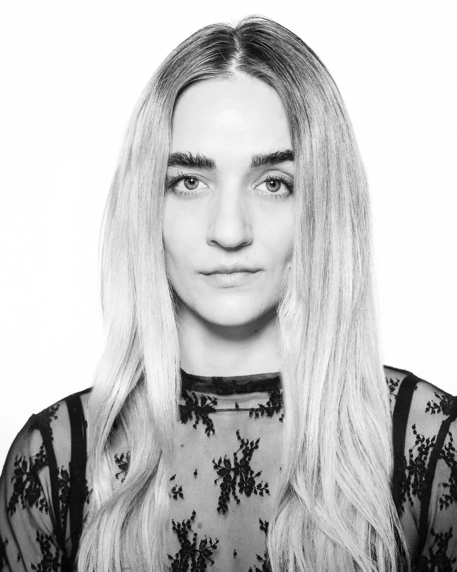 Black and white portrait of a woman with long, straight hair, wearing a sheer top with a floral pattern.