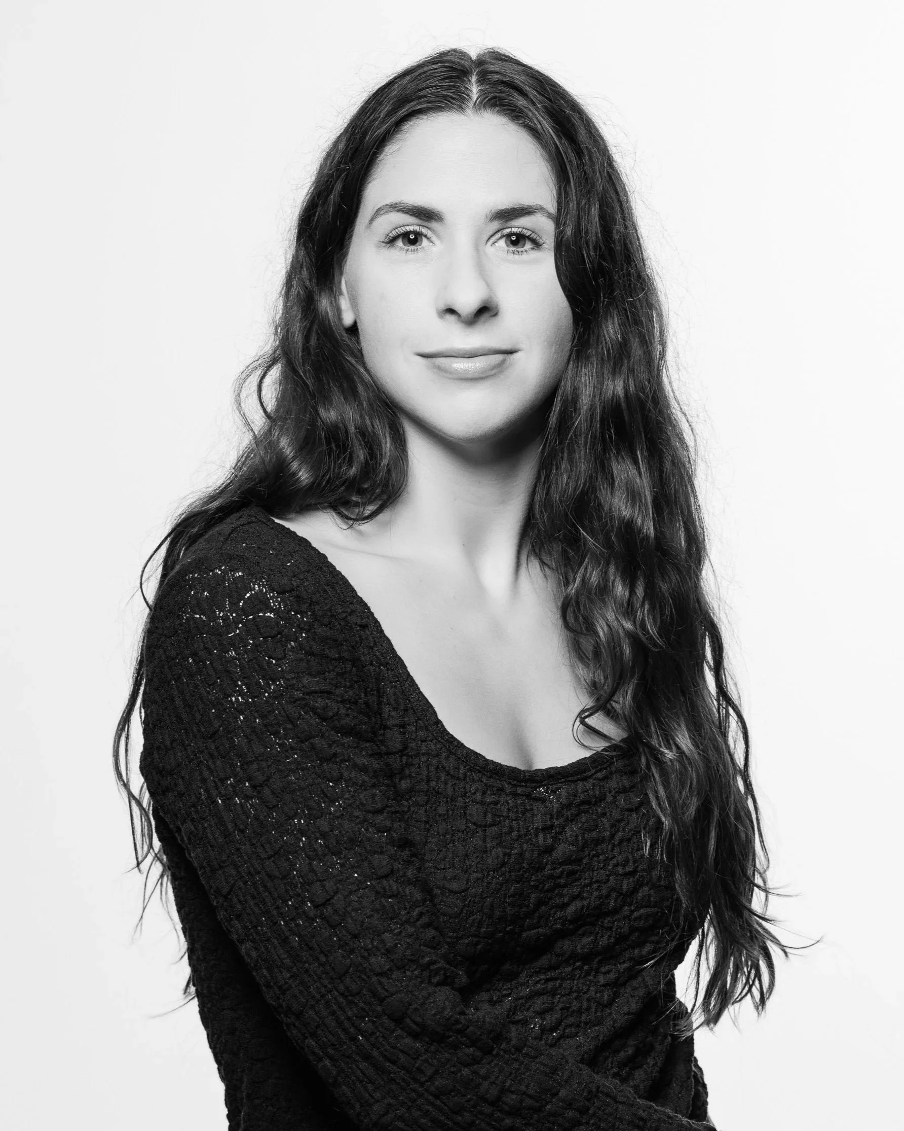 Black-and-white portrait of a woman with long, wavy hair, wearing a black textured top, looking directly at the camera with a slight smile.