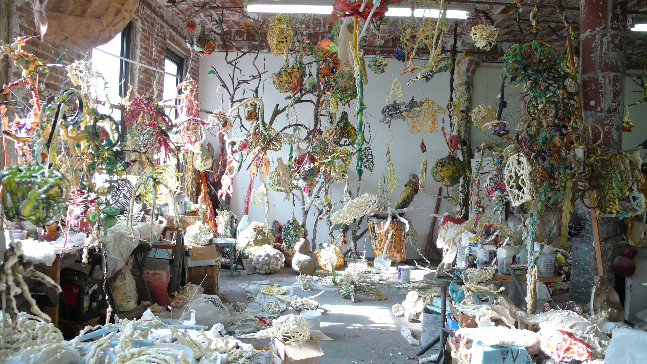 A photo of the inside of Ming Fay's studio space that's absolutely crowded with sculptures, branches, paper pulp and other materials
