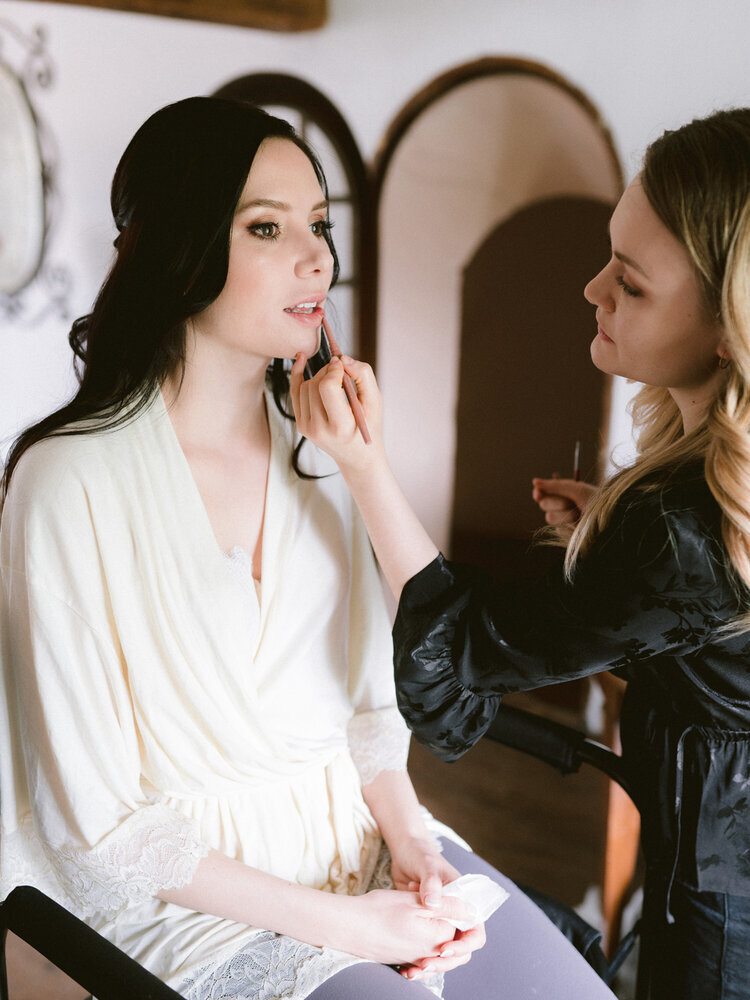  Mallory’sbeing beautified for her French Destination Château Wedding at Château du Vivier - neutral glamour eyes and peachy lip color with dark brown loose wavy hair, wearing her bridal robe before changing into her wedding dress. Make up applied by
