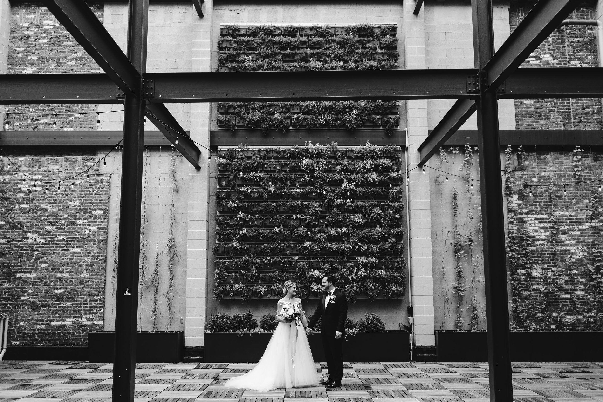 Bride and groom in front of green succulent wall 
