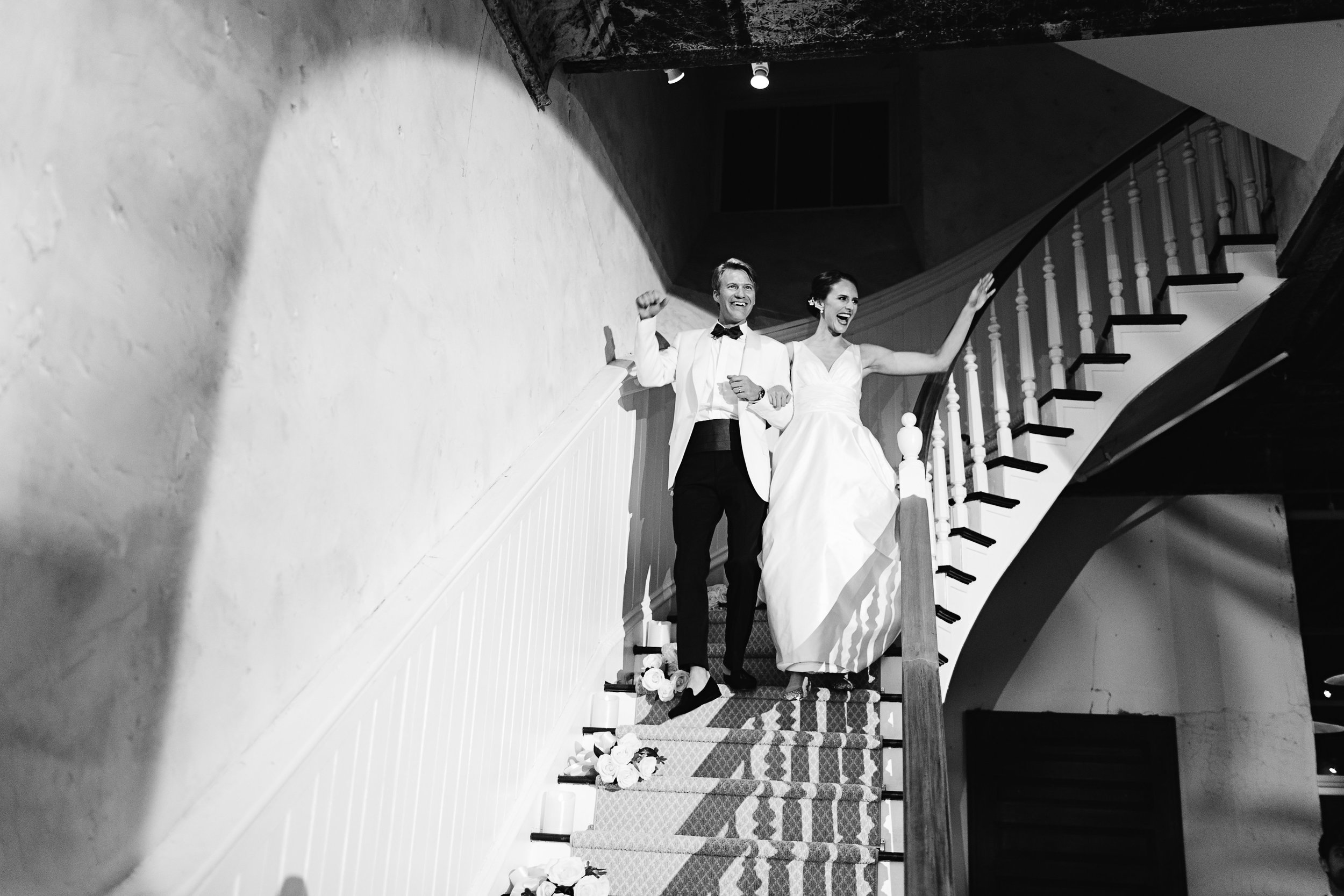 Bride and groom waving to crowd as they descend grand staircase