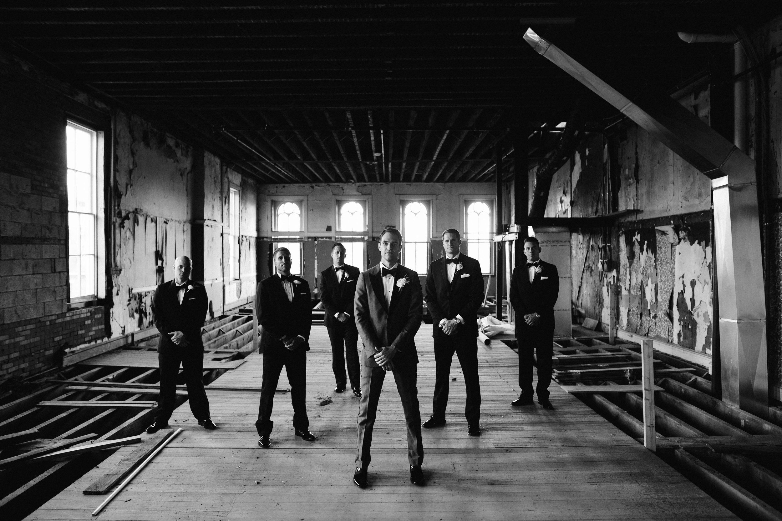 Groom and groomsmen posing in unfinished room black and white