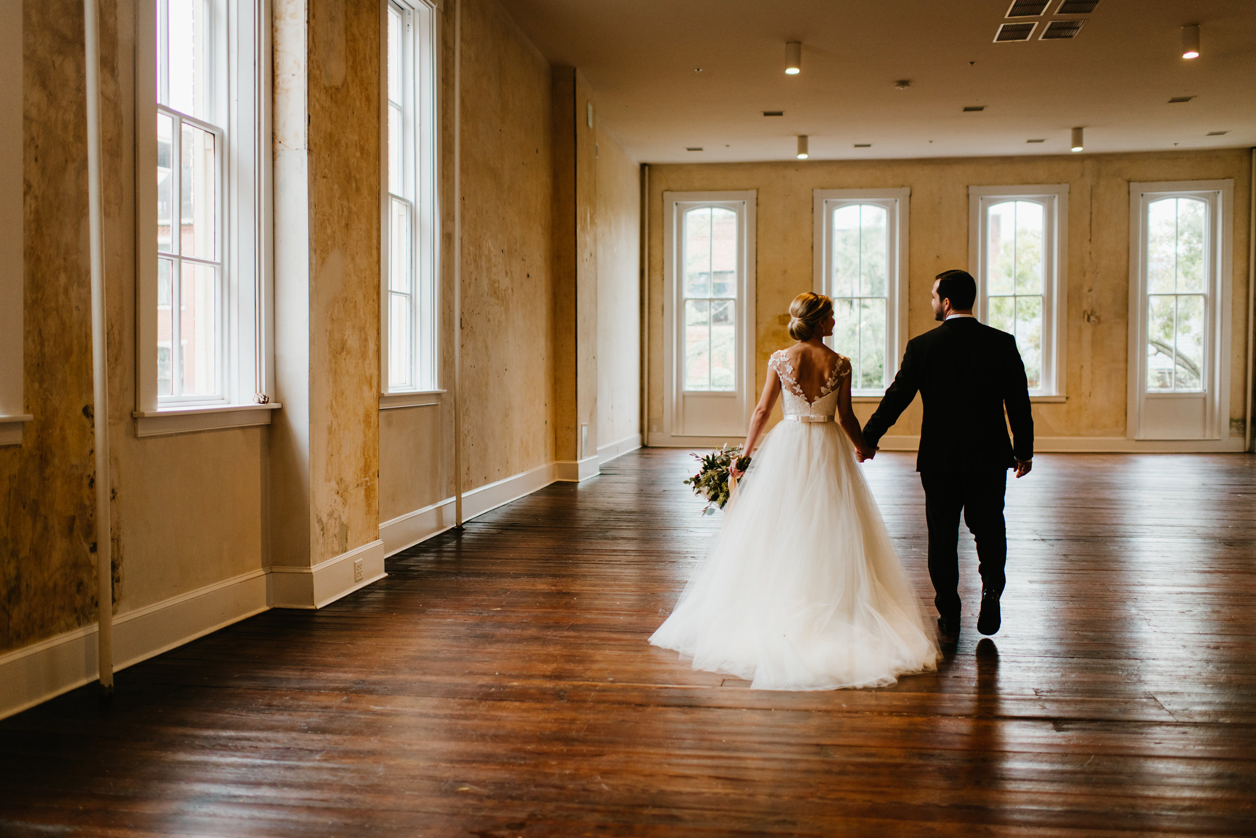 Bride and groom walking in Empire Room towards large windows