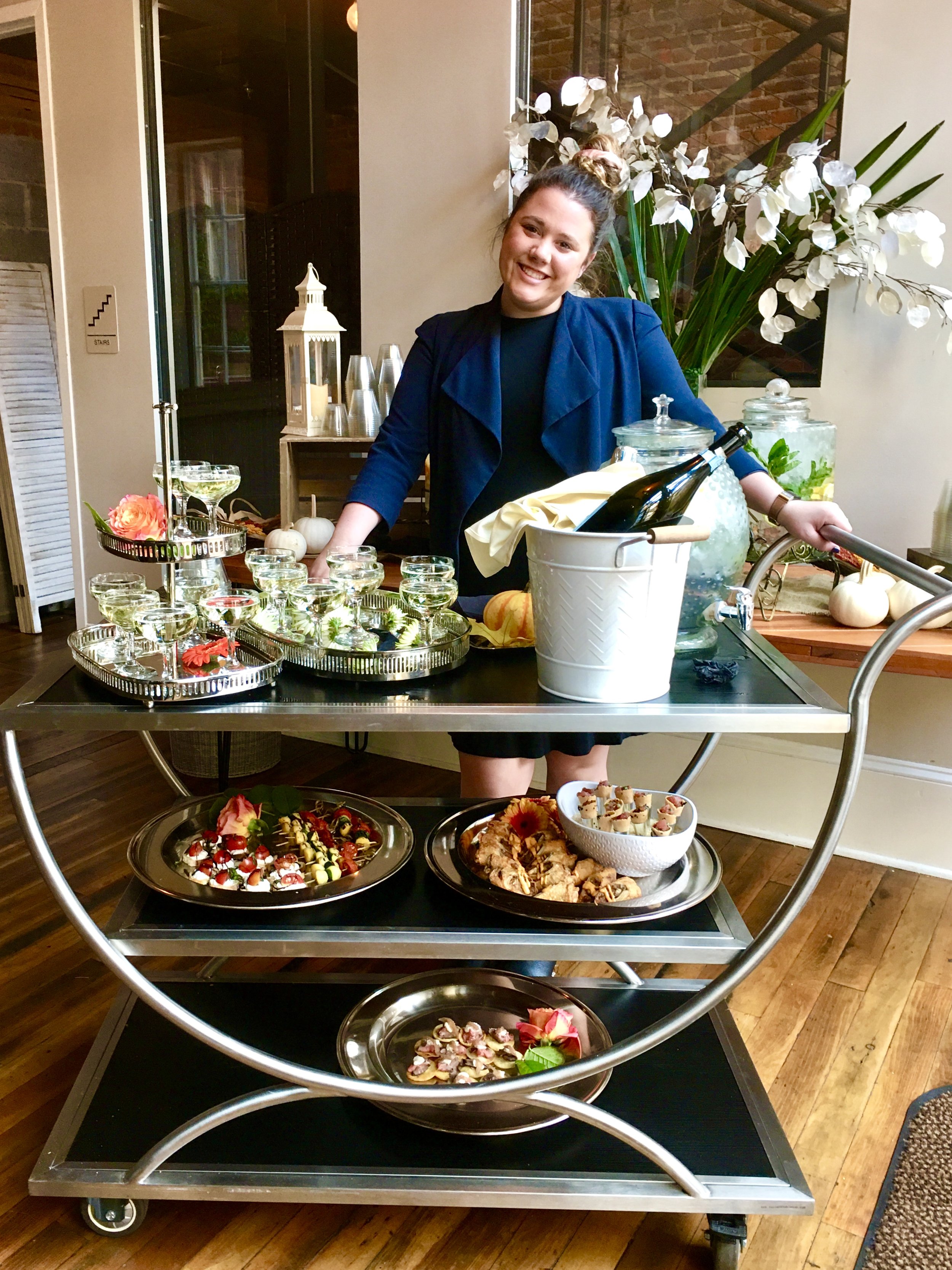 Woman smiling presenting gourmet appetizers and drinks on modern chic cart