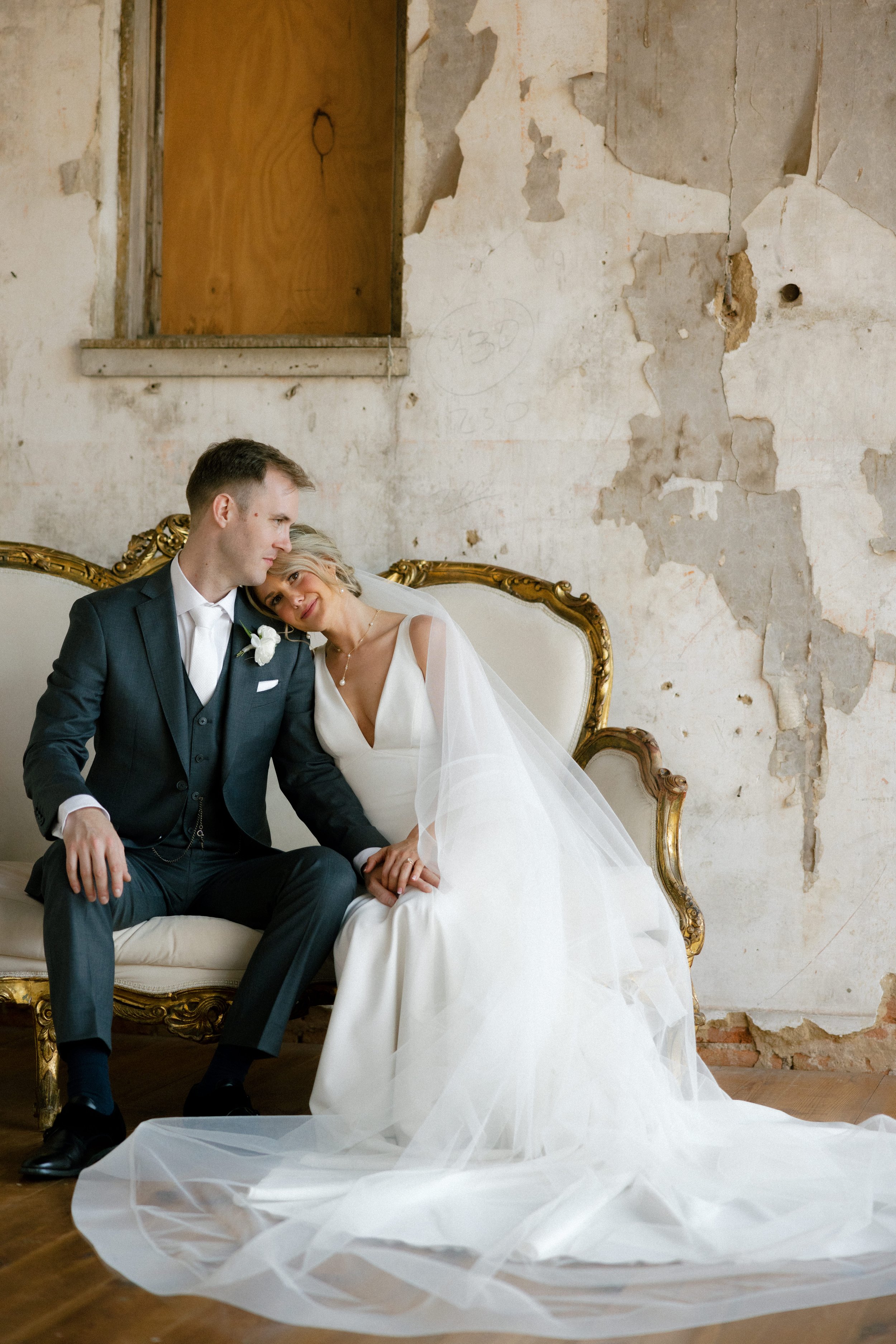 Bride resting head on groom's shoulder on loveseat in rustic room