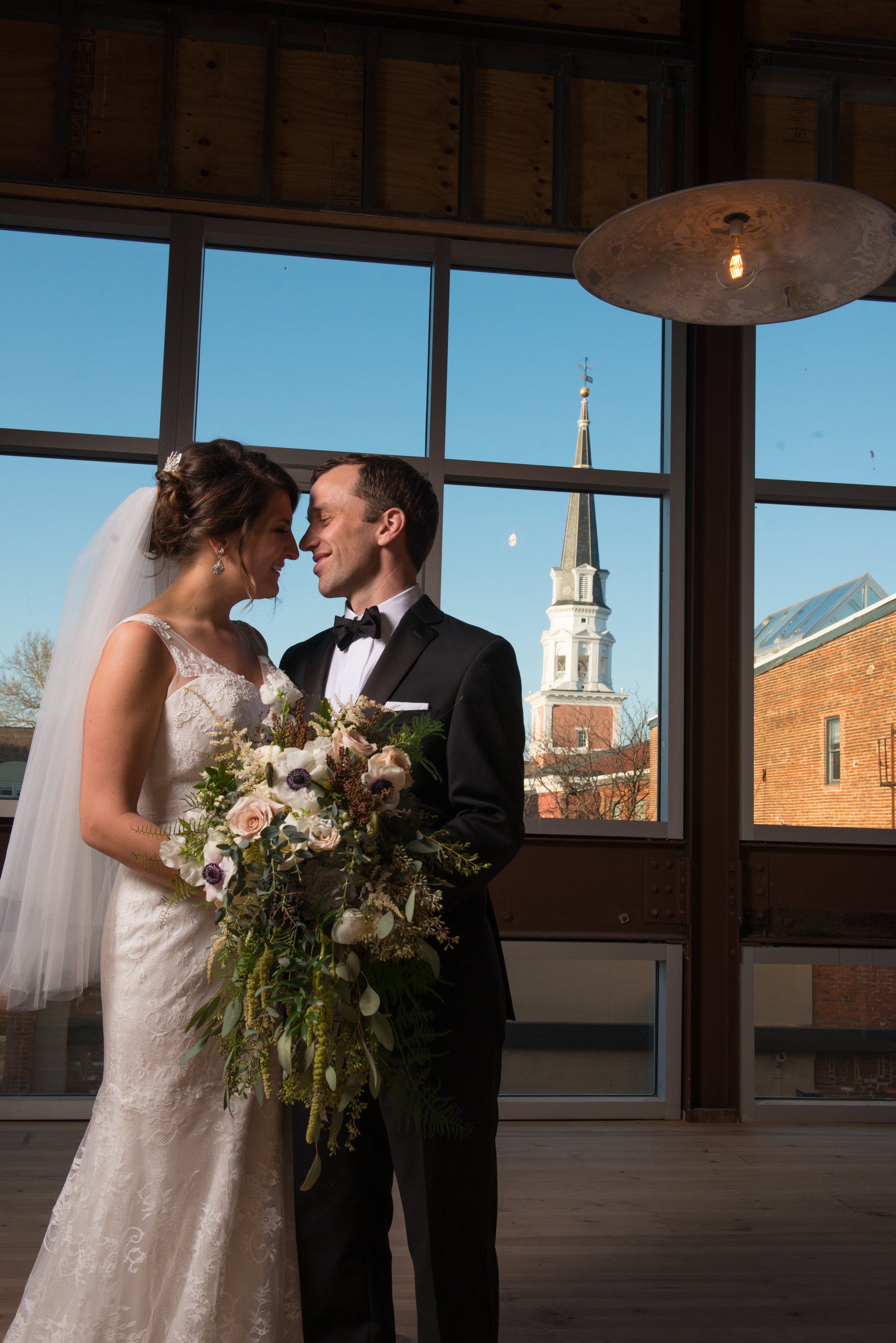 Bride and groom in front of large window with church in background