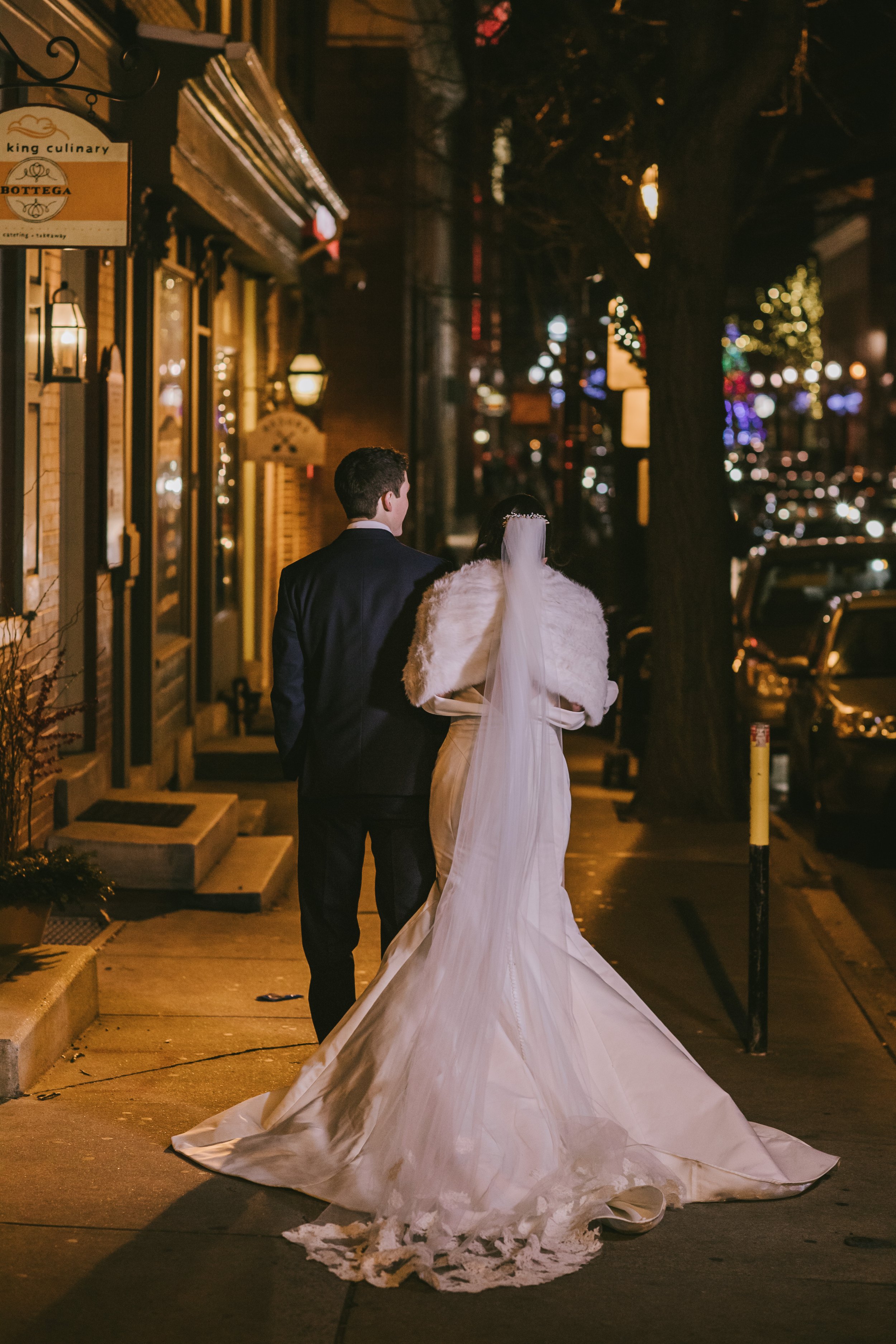 View from behind of bride and groom walking sidewalk at night