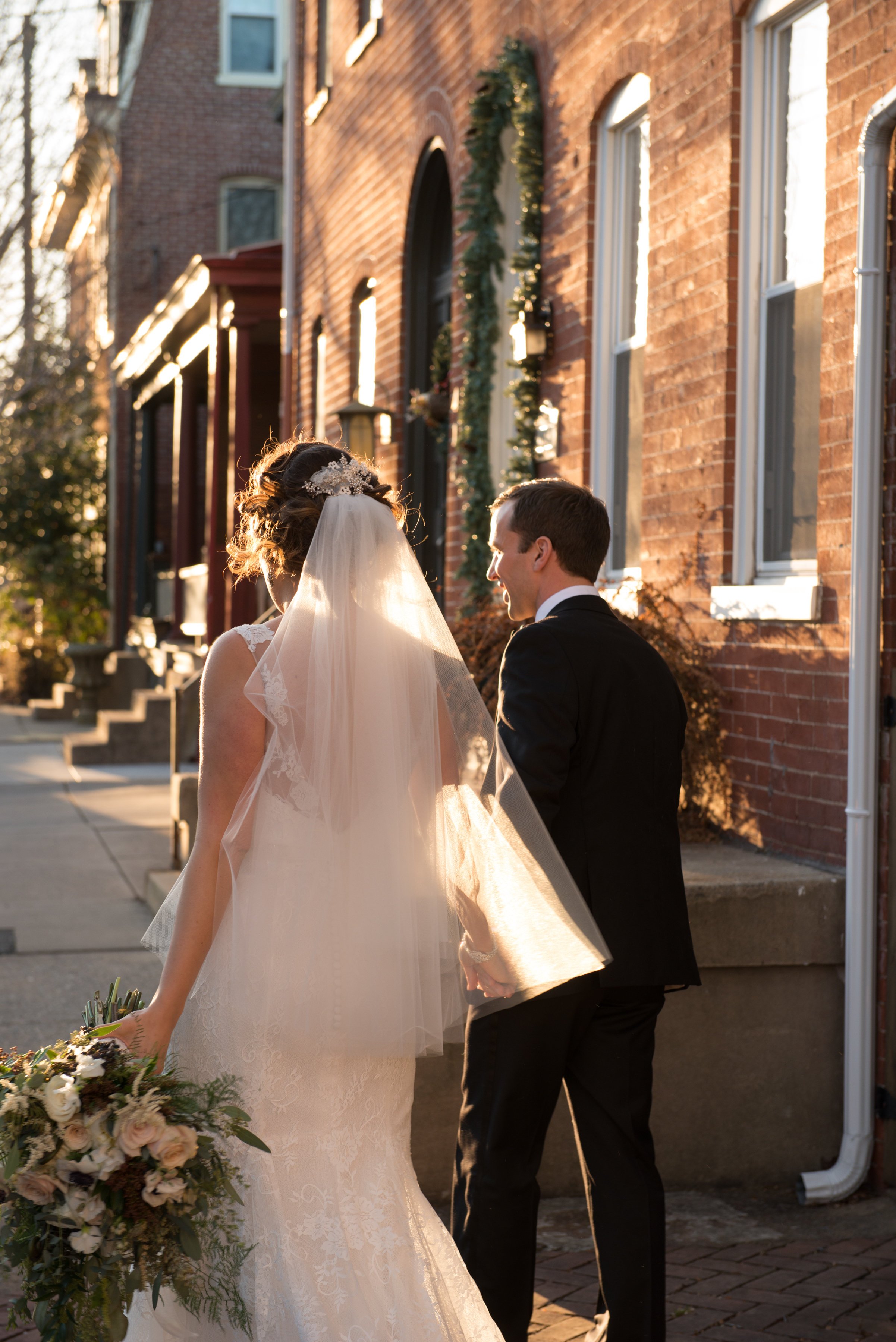 Bride and groom walking during golden hour on brick house lined street Lancaster center city