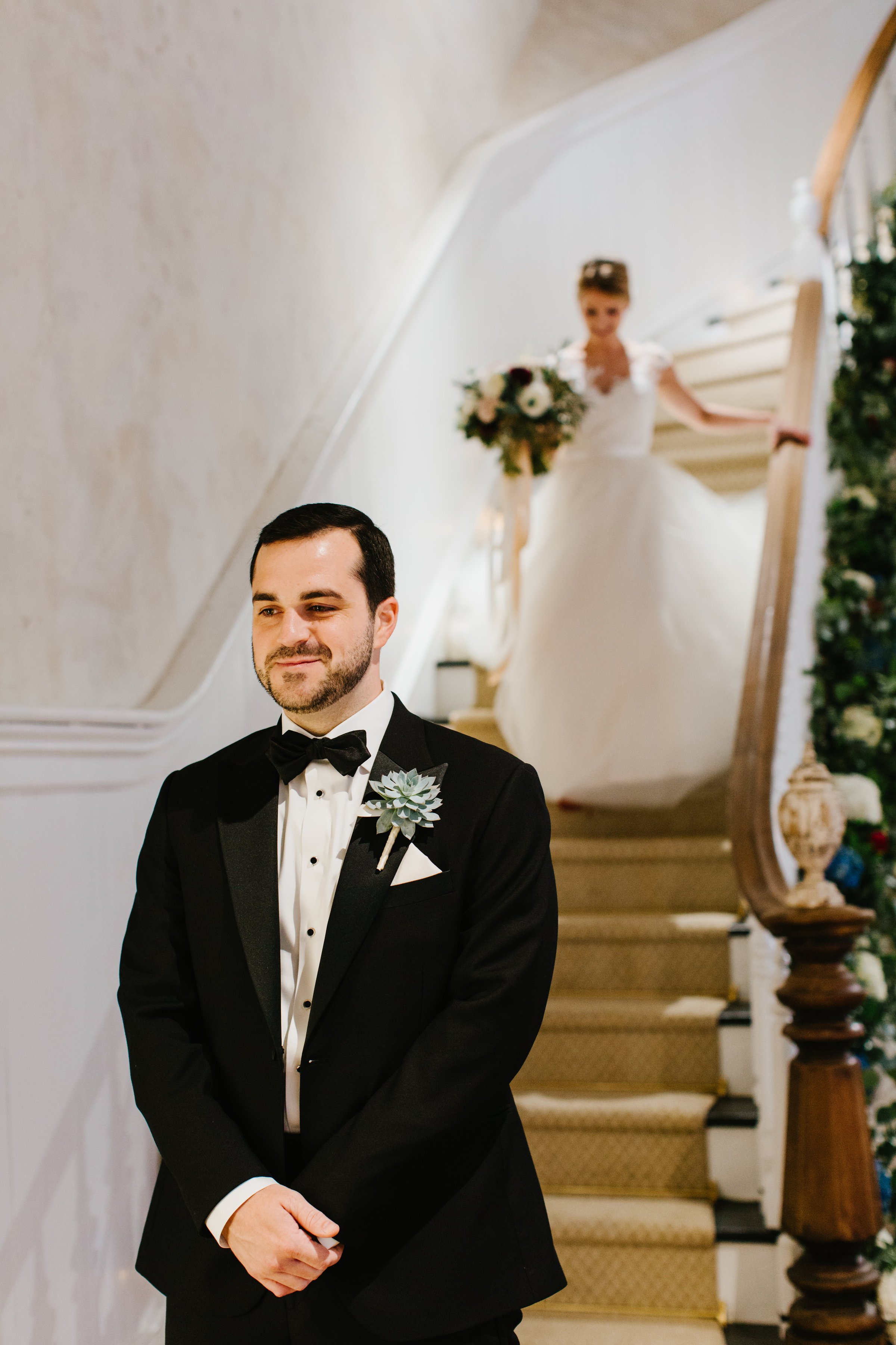 Groom waiting at bottom of grand staircase for bride