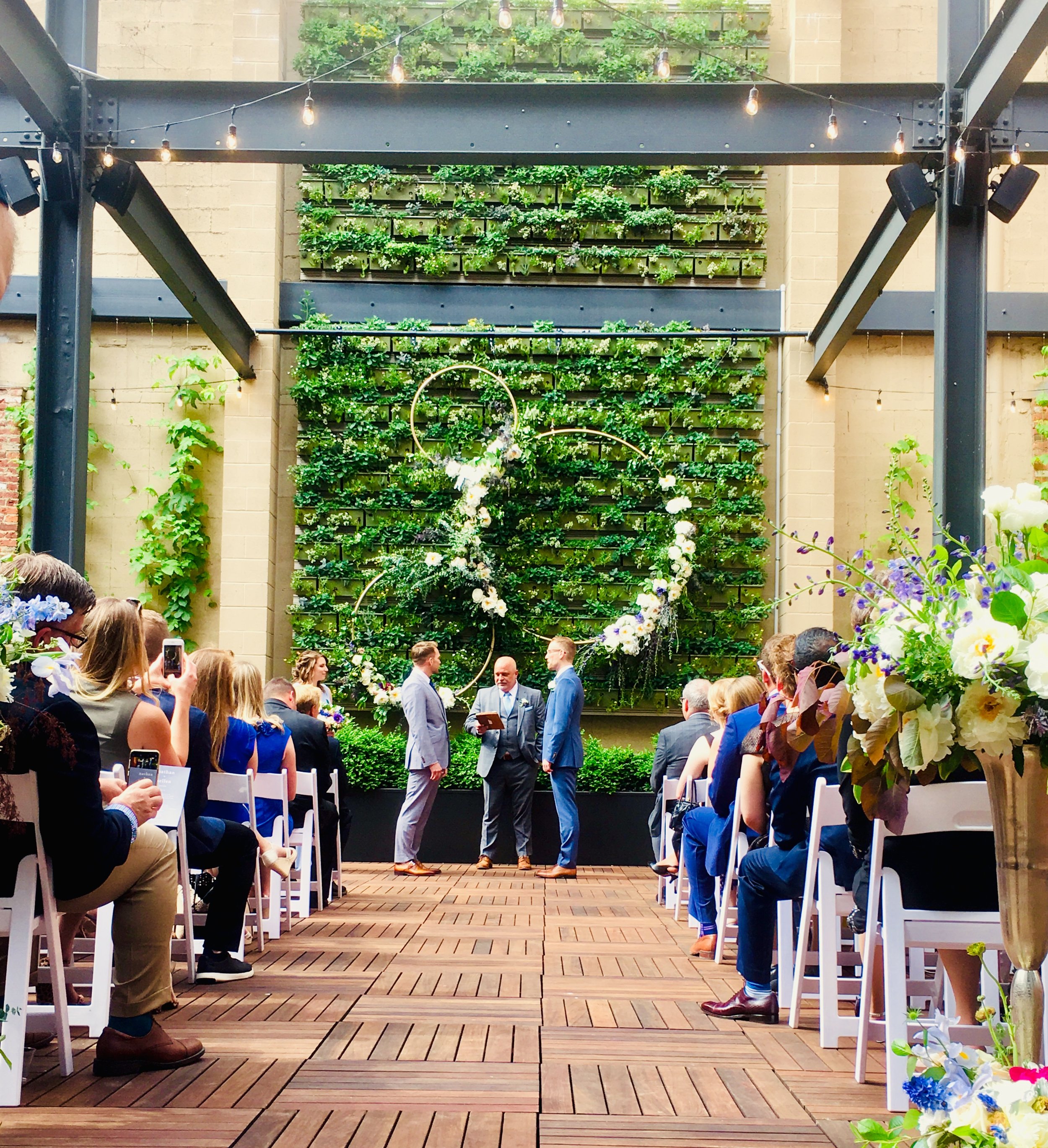 Ceremony on outdoor Terrace circled floral arches in front of green succulent wall