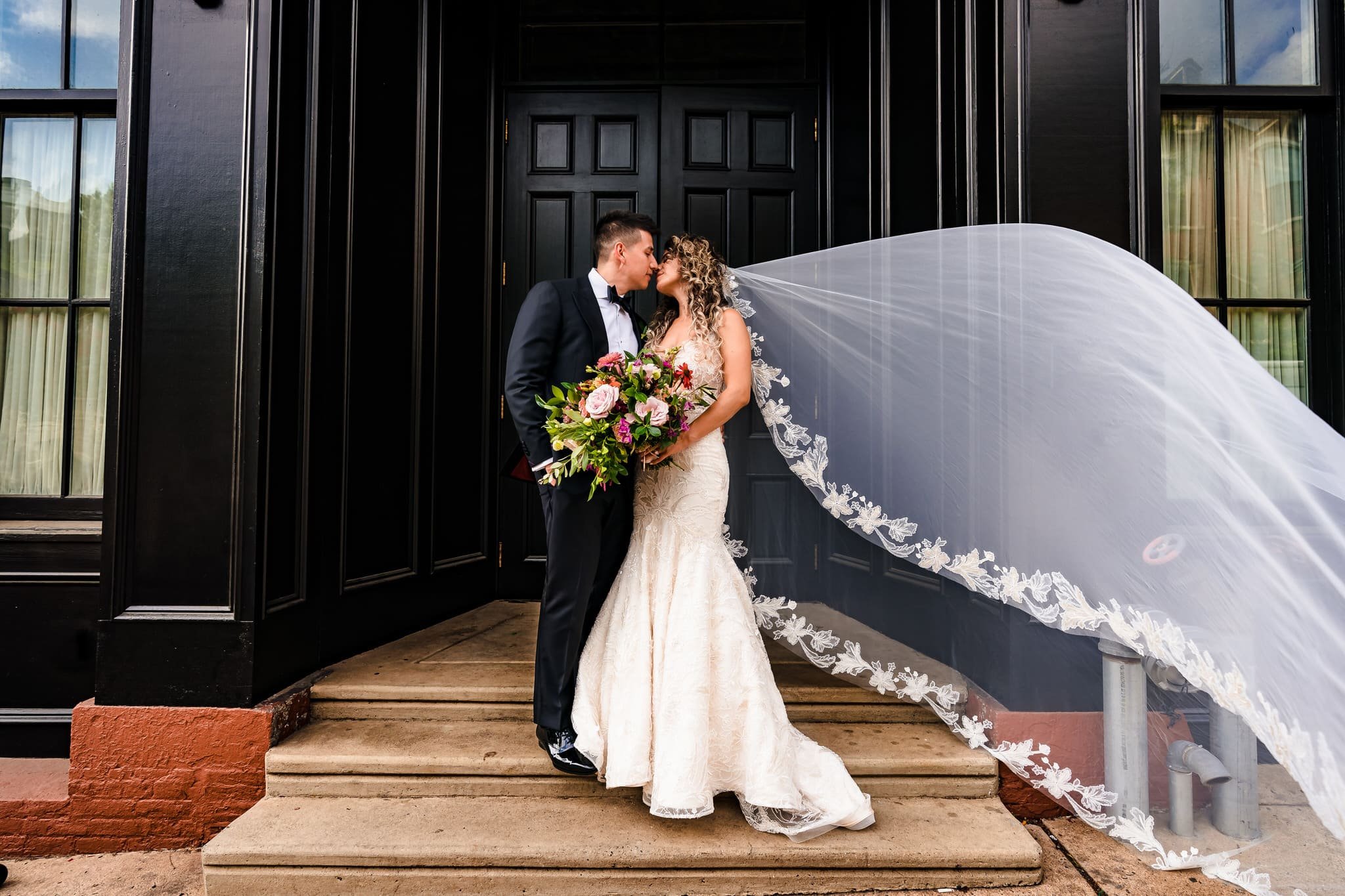 Groom and bride with veil lifted in front of black door of Excelsior