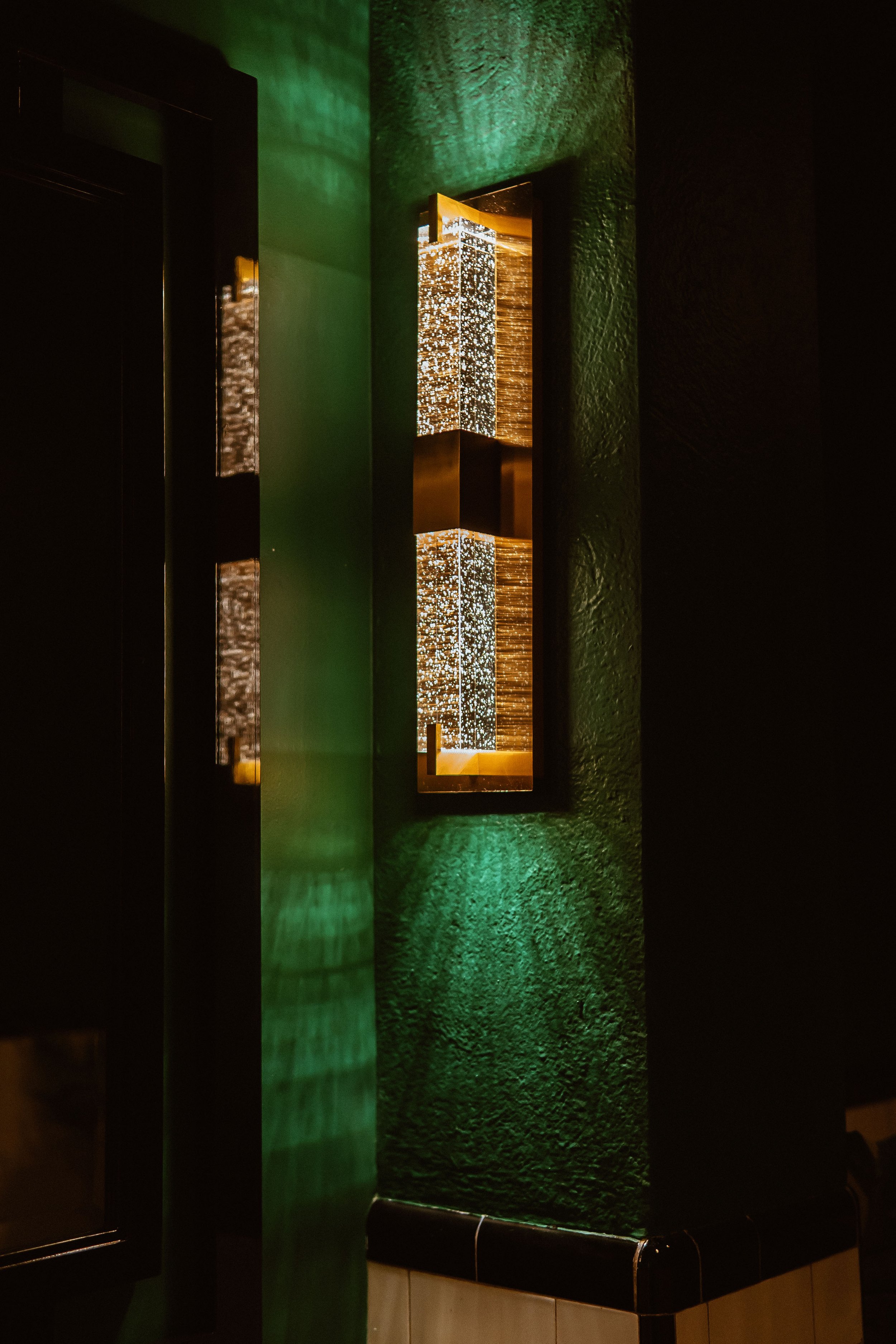 Eclectic bubbled glass wall light glowing on emerald walls