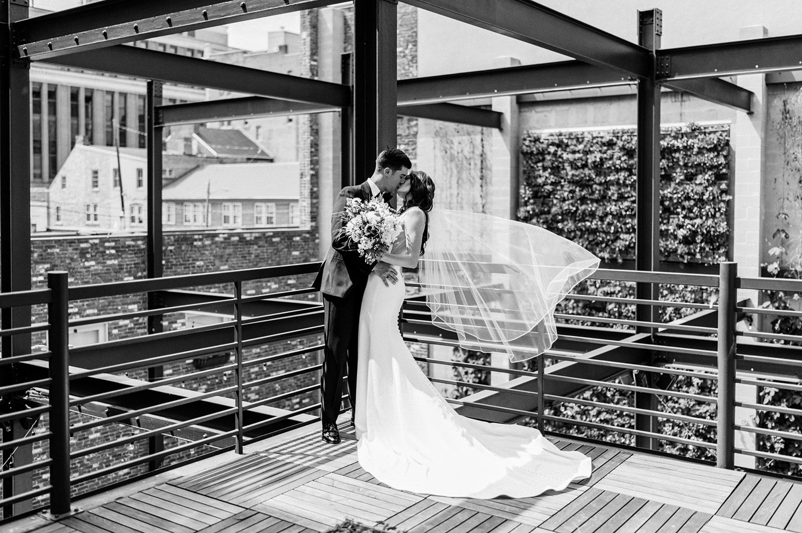 Bride and groom on rooftop deck industrial beams in front of greenery succulent wall