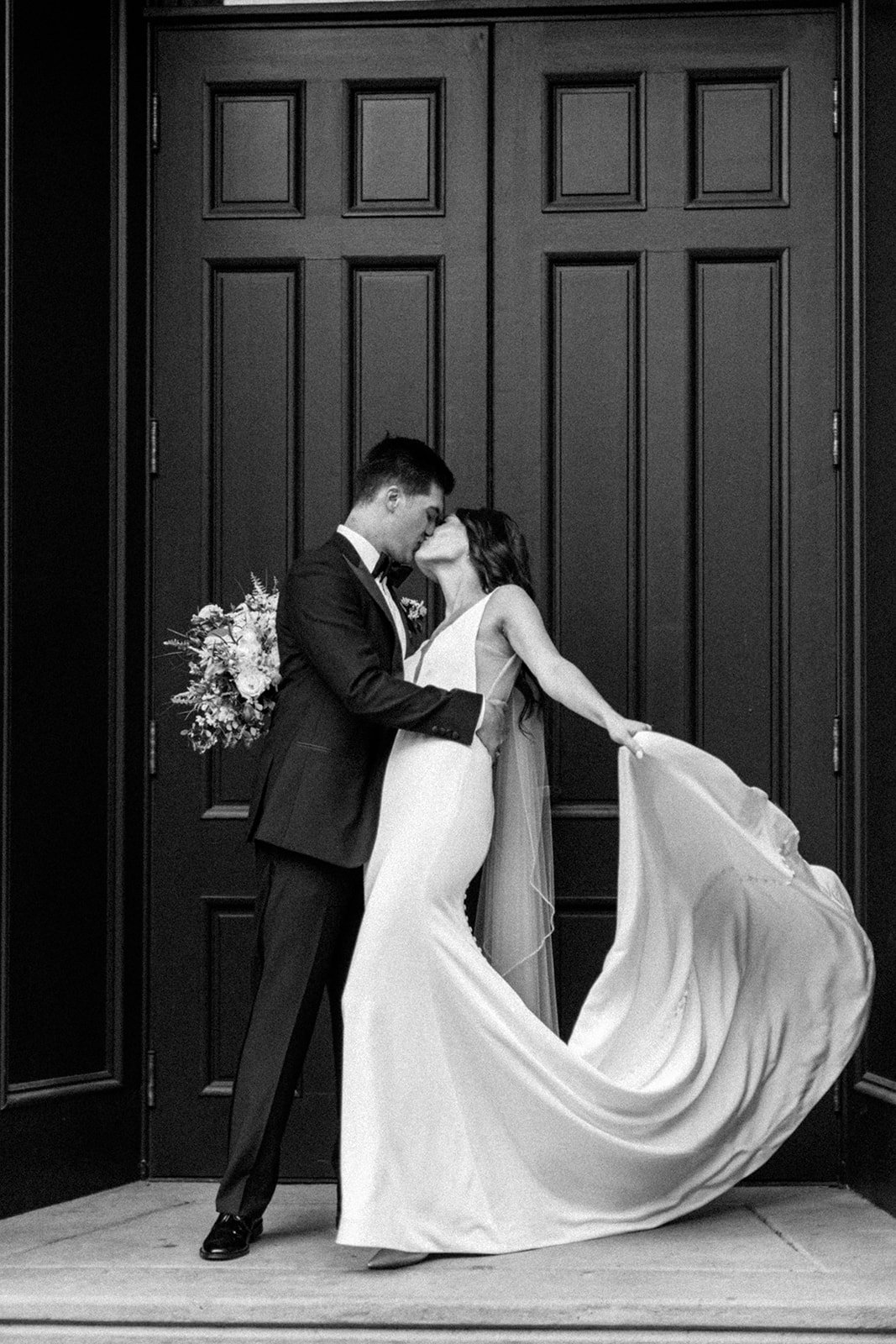 Bride and groom kiss in front of black exterior doors at Excelsior