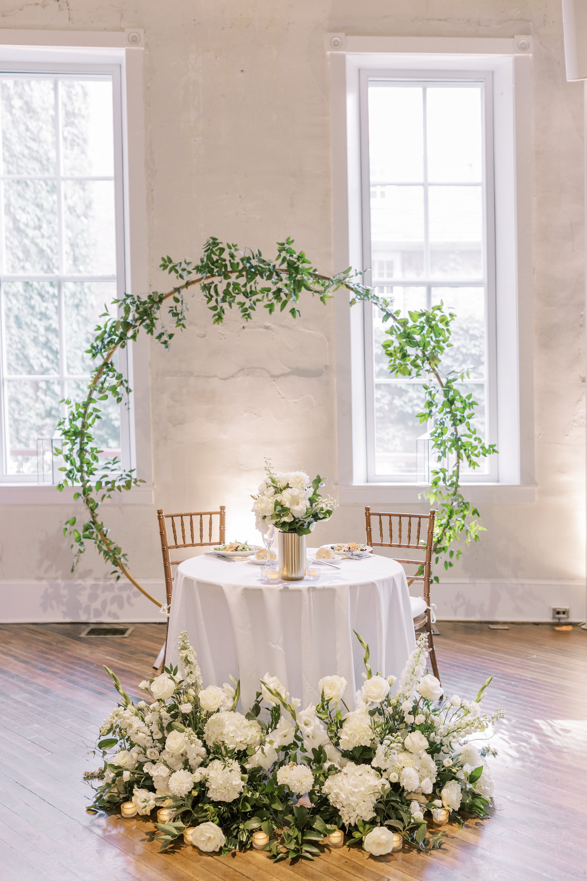 White wedding reception sweetheart table with greenery arch and rose pile