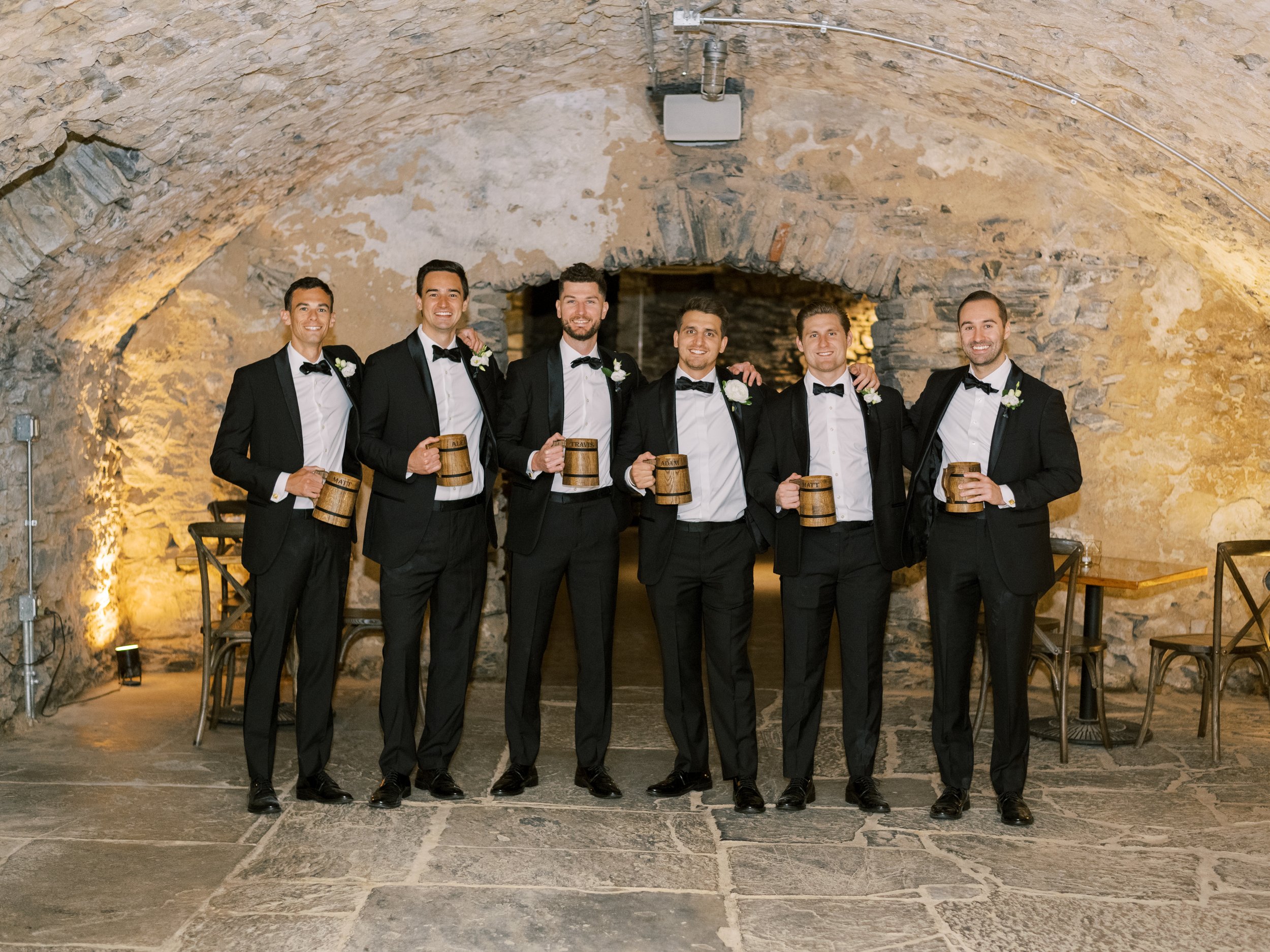 Groom and groomsmen holding beer mugs in catacombs of Excelsior wedding venue