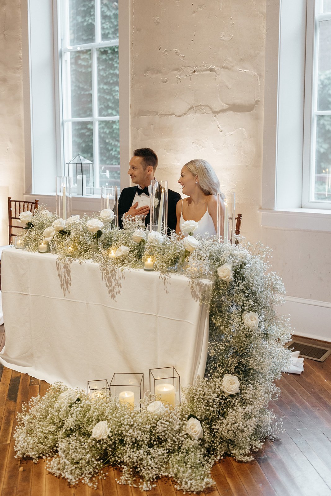 Bride and groom seated at table with large display of baby's breath and candles