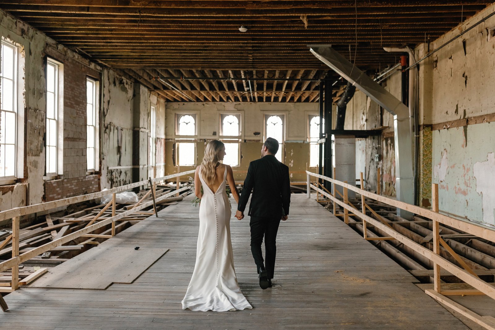 Bride and groom walking in unfinished antique historic room with large windows