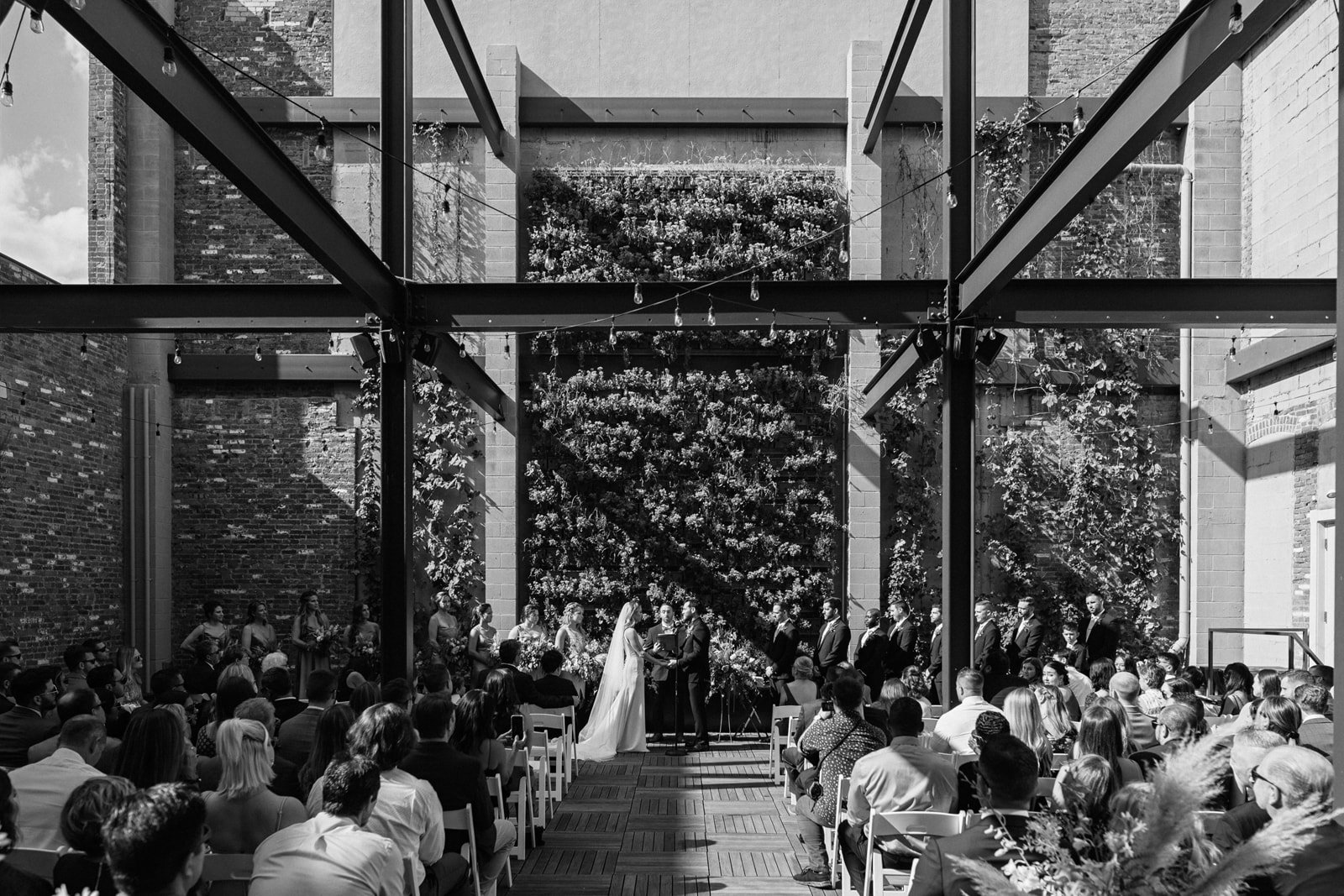 Black and white photo of ceremony in the Terrace in front of green succulent wall