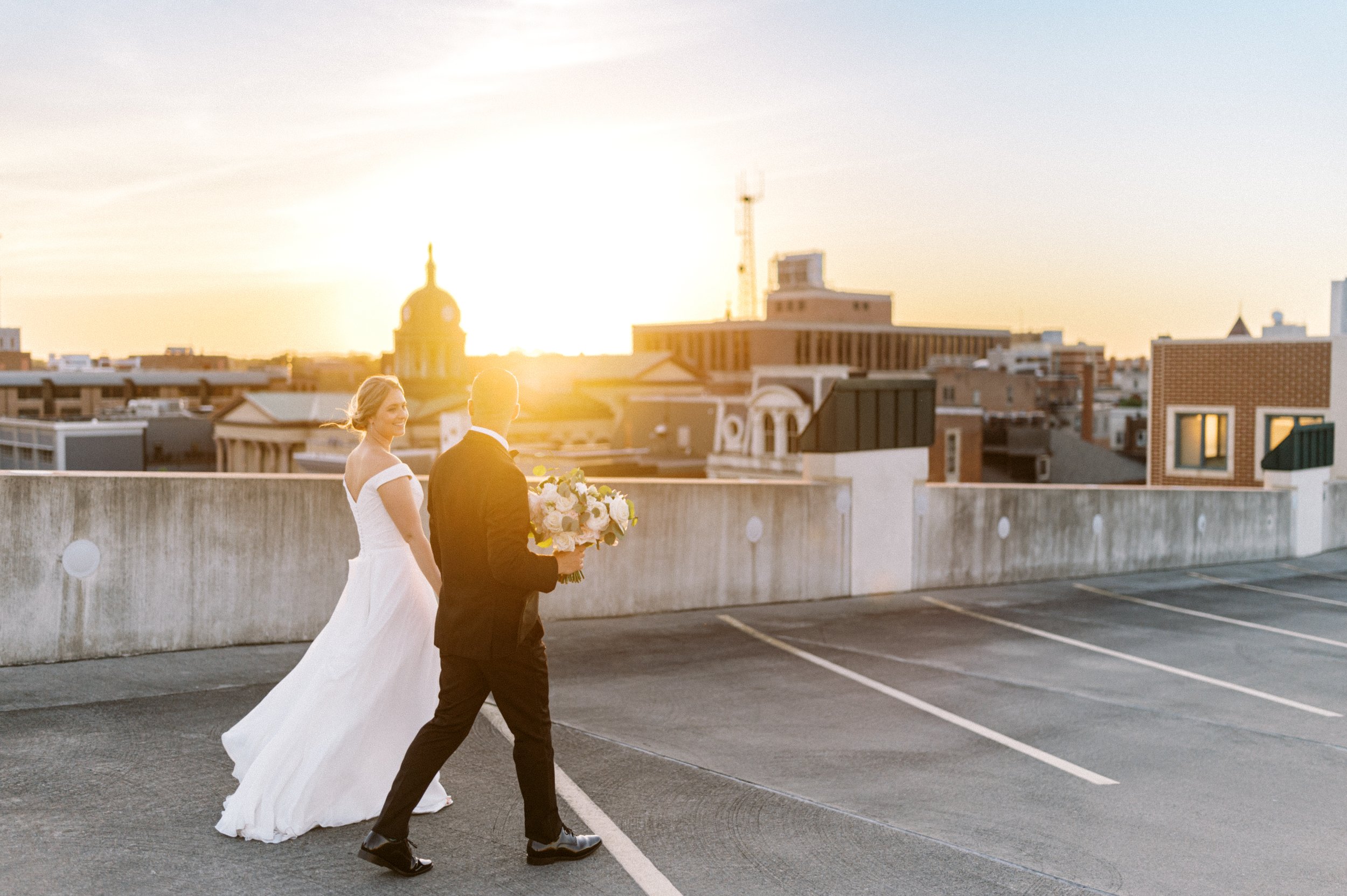 Bride and groom walking on parking garage roof top at sunset