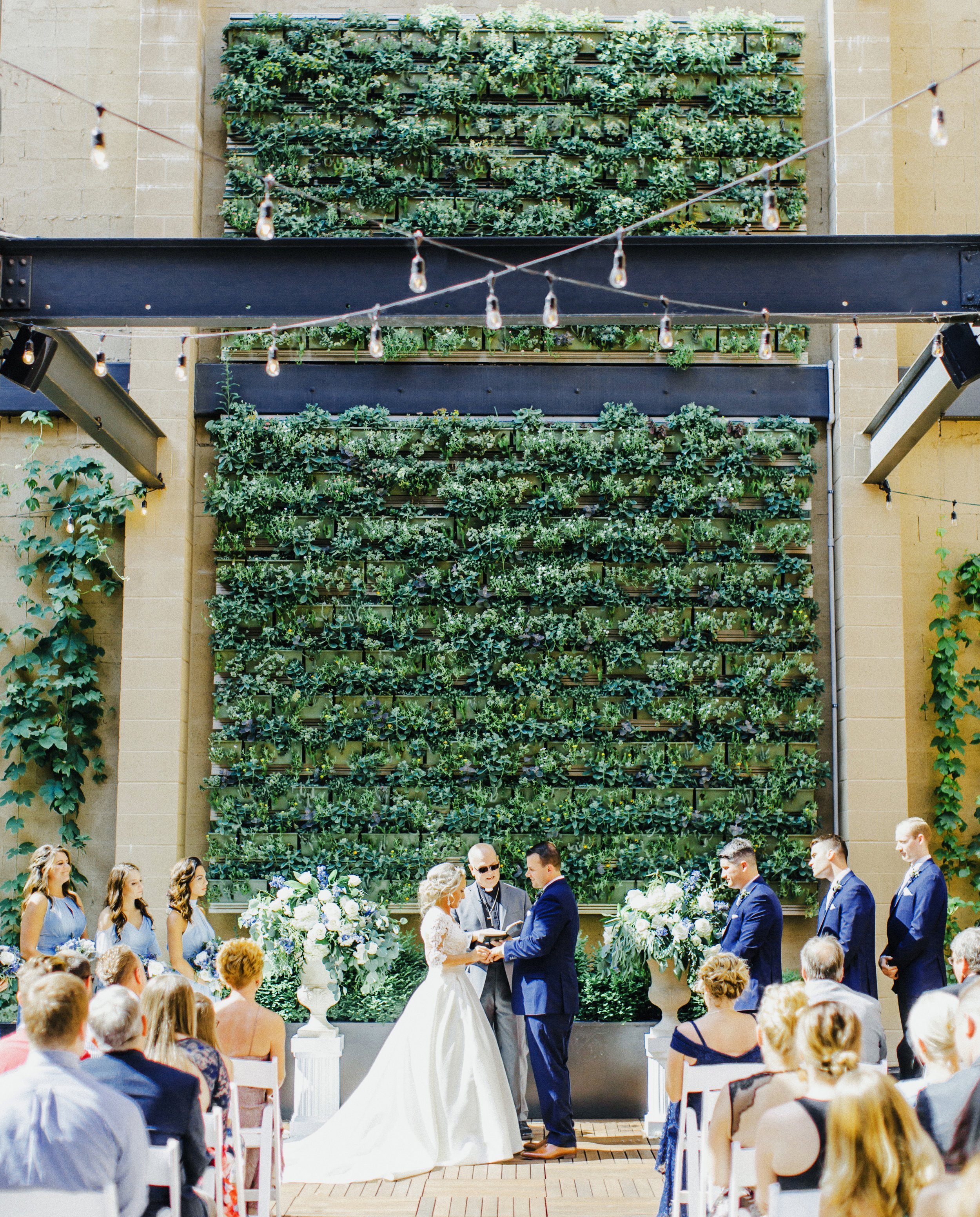 Bride and groom exchanging vows in front of green succulent wall on Terrace of Excelsior venue