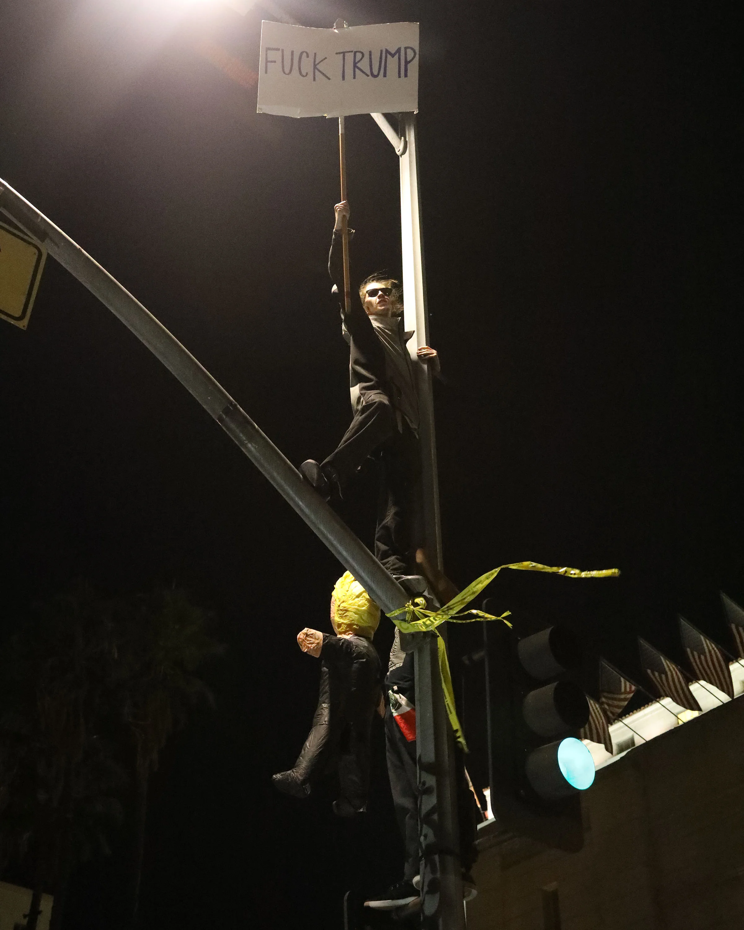 A protester holds up his sign to the croud atop of a street sign in front of Los Angeles City Hall at the protest held in response to the outcome of the presidential election in Downtown Los Angeles on Nov. 9, 2016