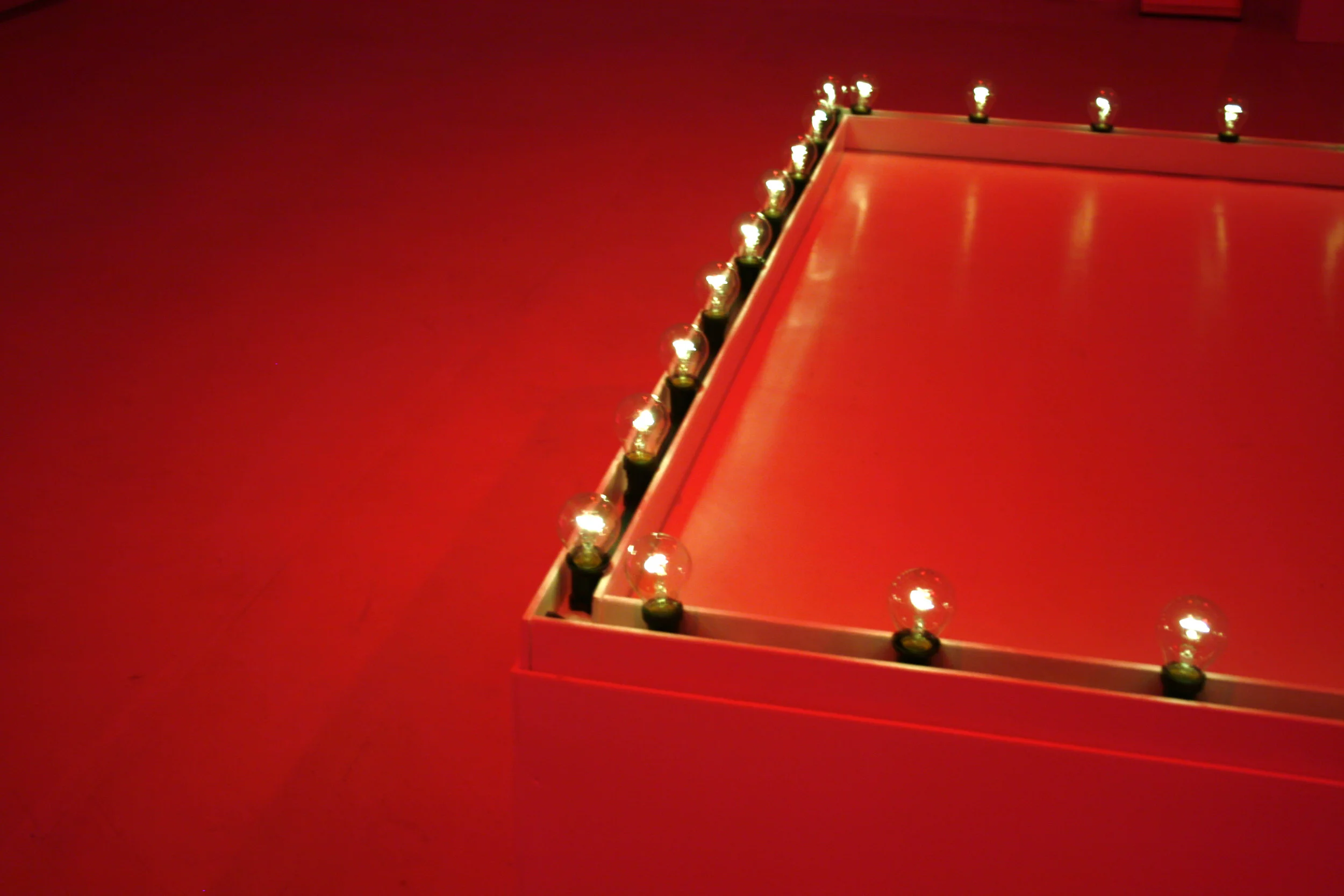   POSTURES A-TO-M (from LONE DUETS)  Live performance   Material  4 hour durational performance with latex pig mask, apple core, bandage, red fluorescent strip lights, vaseline, and white plinth with electric light bulbs.  A solo choreographed betwee